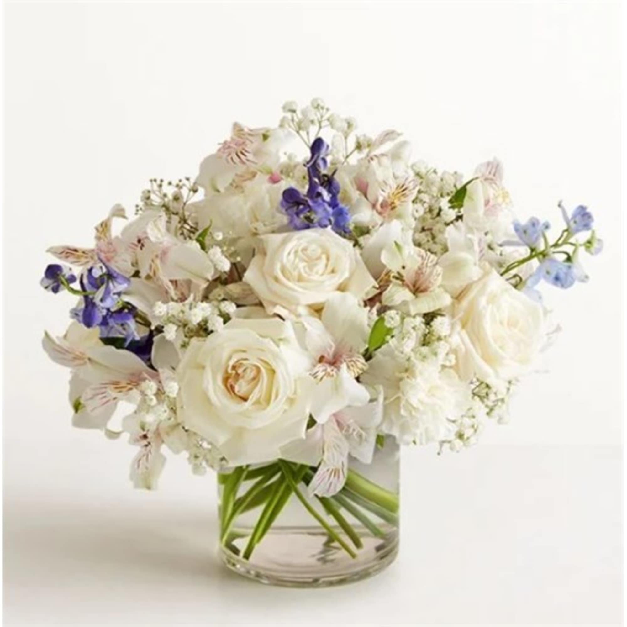 White rose bouquet with purple and pale pink flowers in a clear glass vase