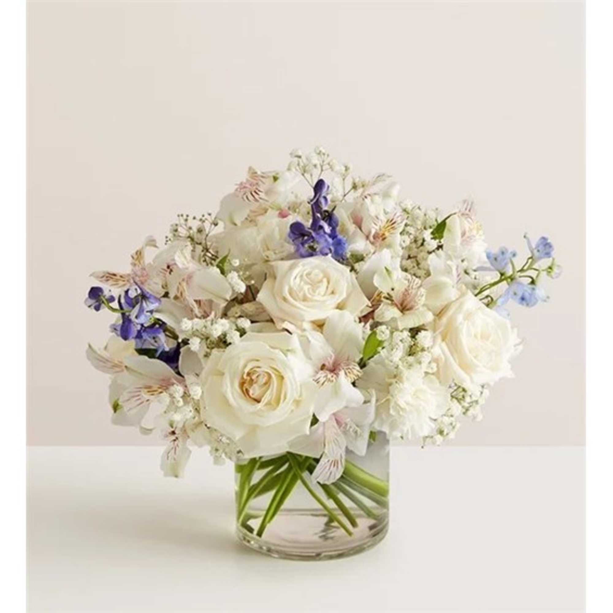 White rose bouquet with small purple and blue flowers in a clear glass vase