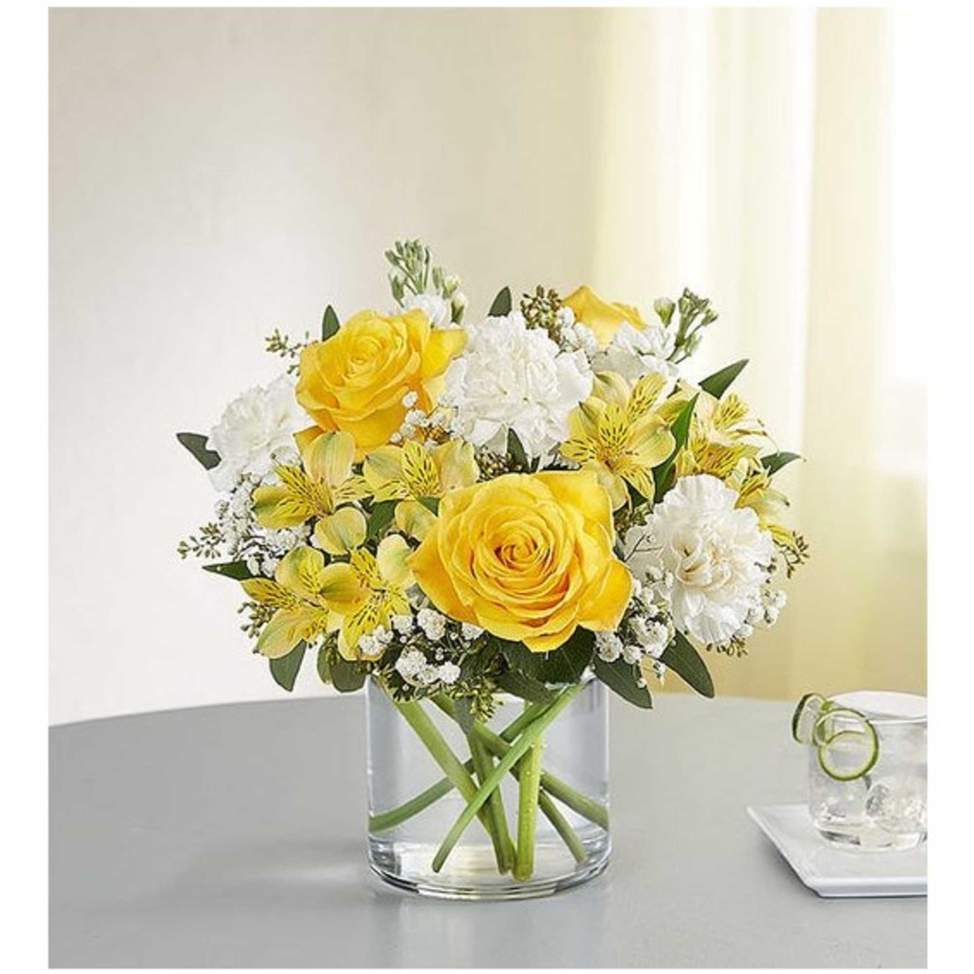 Yellow roses and white flowers arranged in a clear glass vase