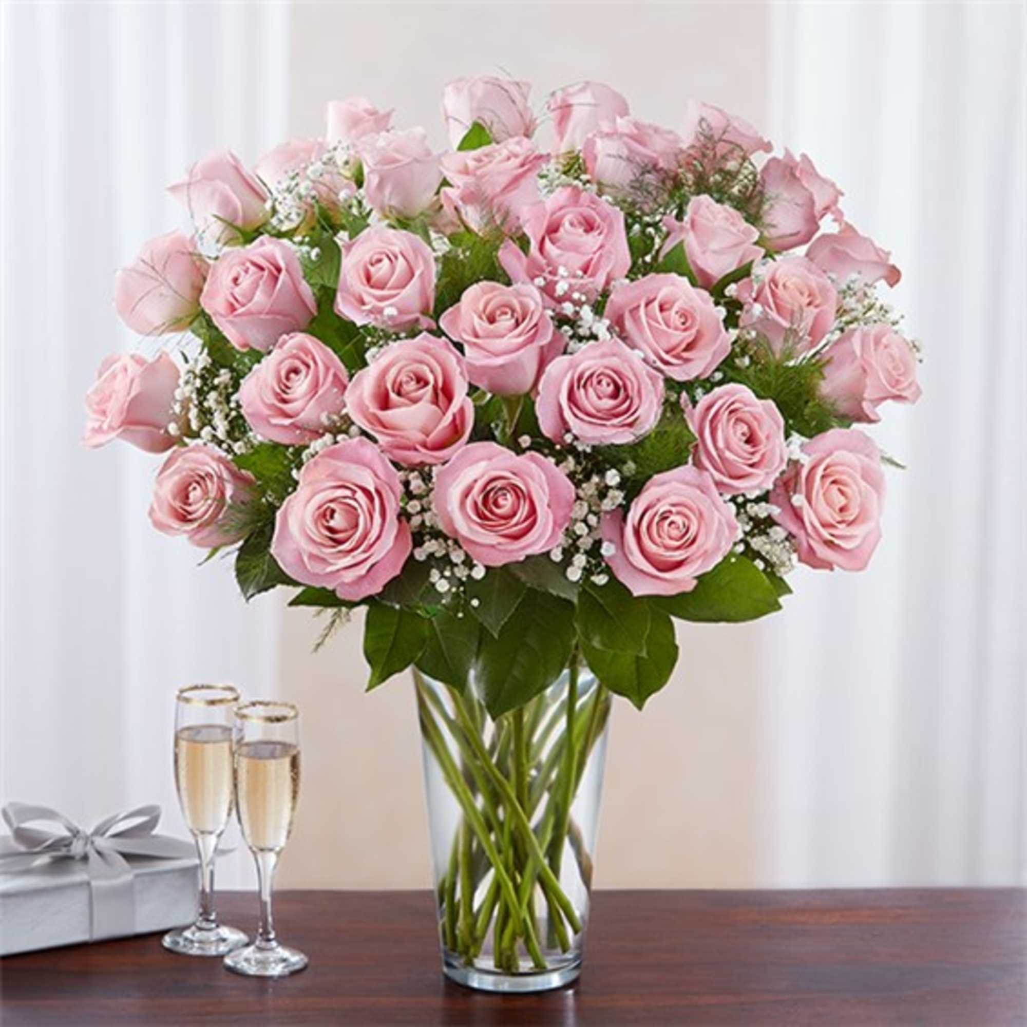 Bouquet of pink roses in a clear glass vase with a gift box and champagne flutes