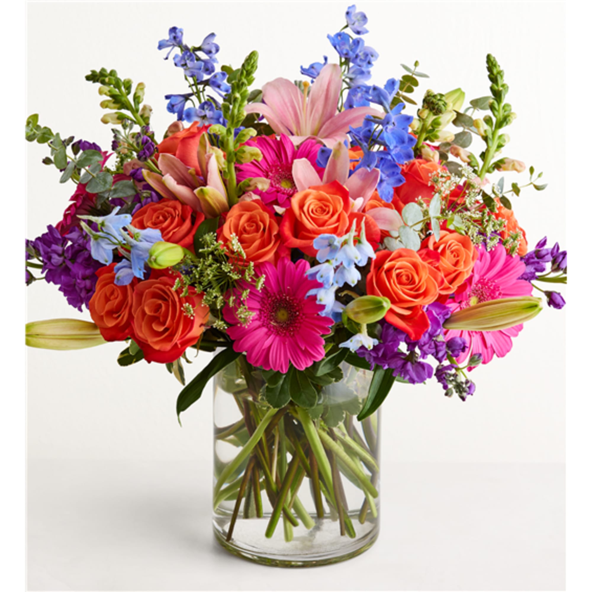 Bright mixed bouquet of roses, lilies, and daisies in a clear glass vase