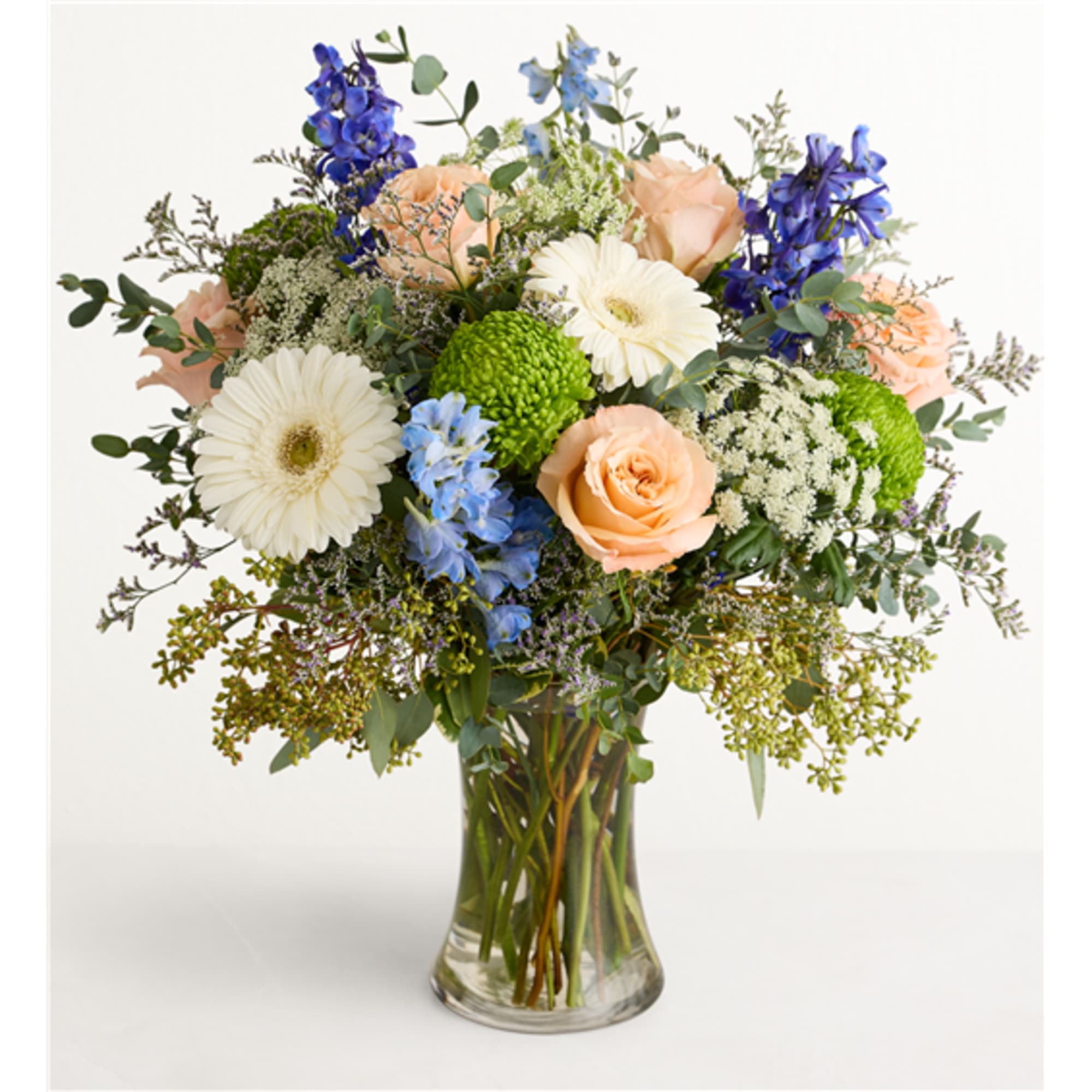 Mixed bouquet of peach roses, white gerberas, and blue flowers in a glass vase