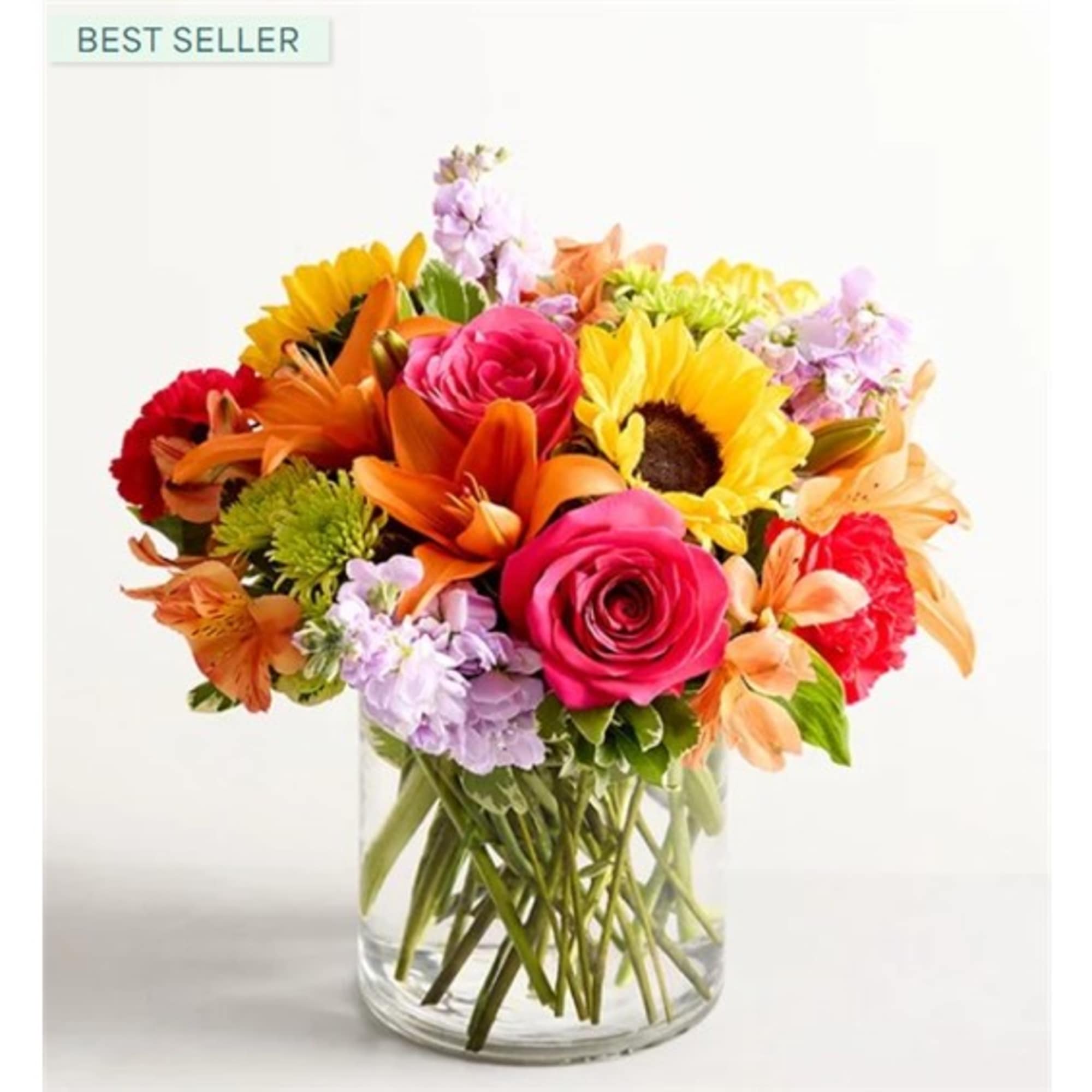Mixed bouquet of roses, sunflowers, lilies, and carnations in a clear glass vase