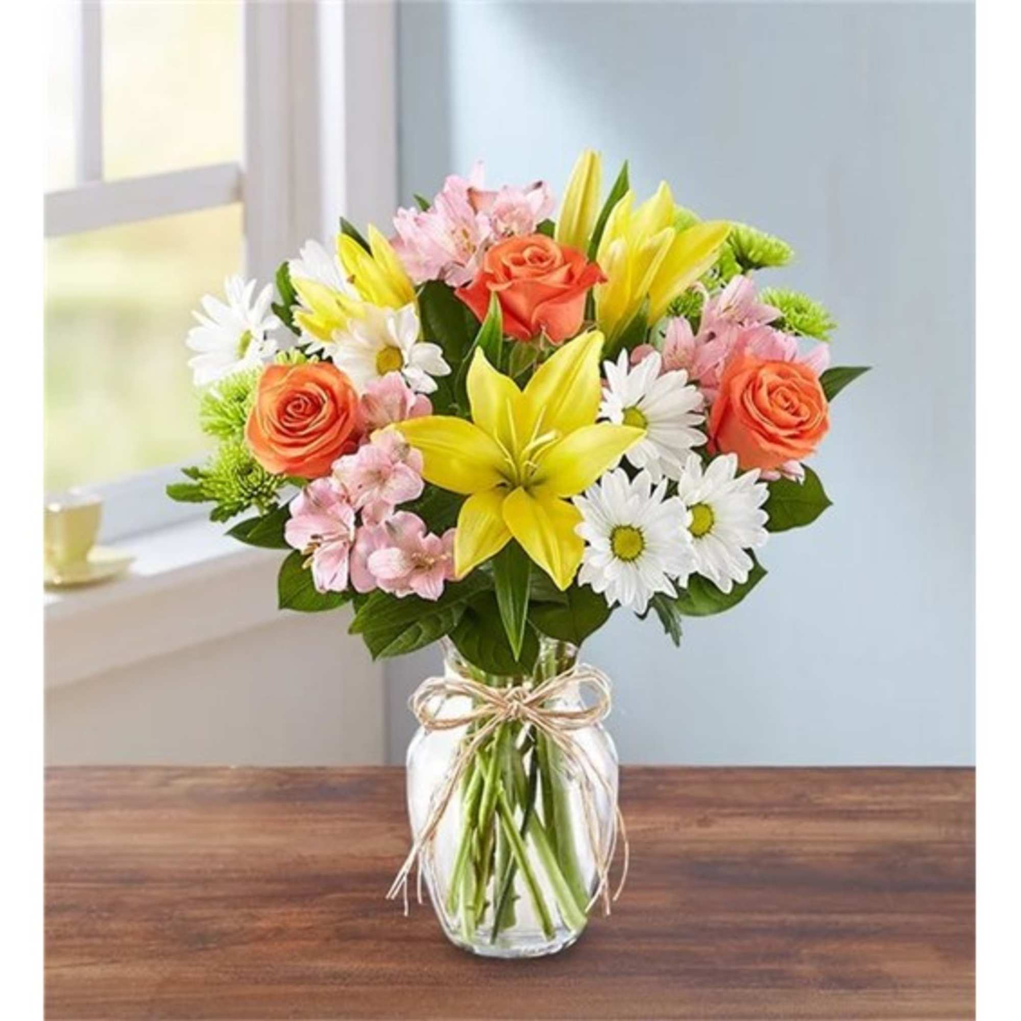 Bouquet of yellow lilies, orange roses, and white daisies in a glass vase