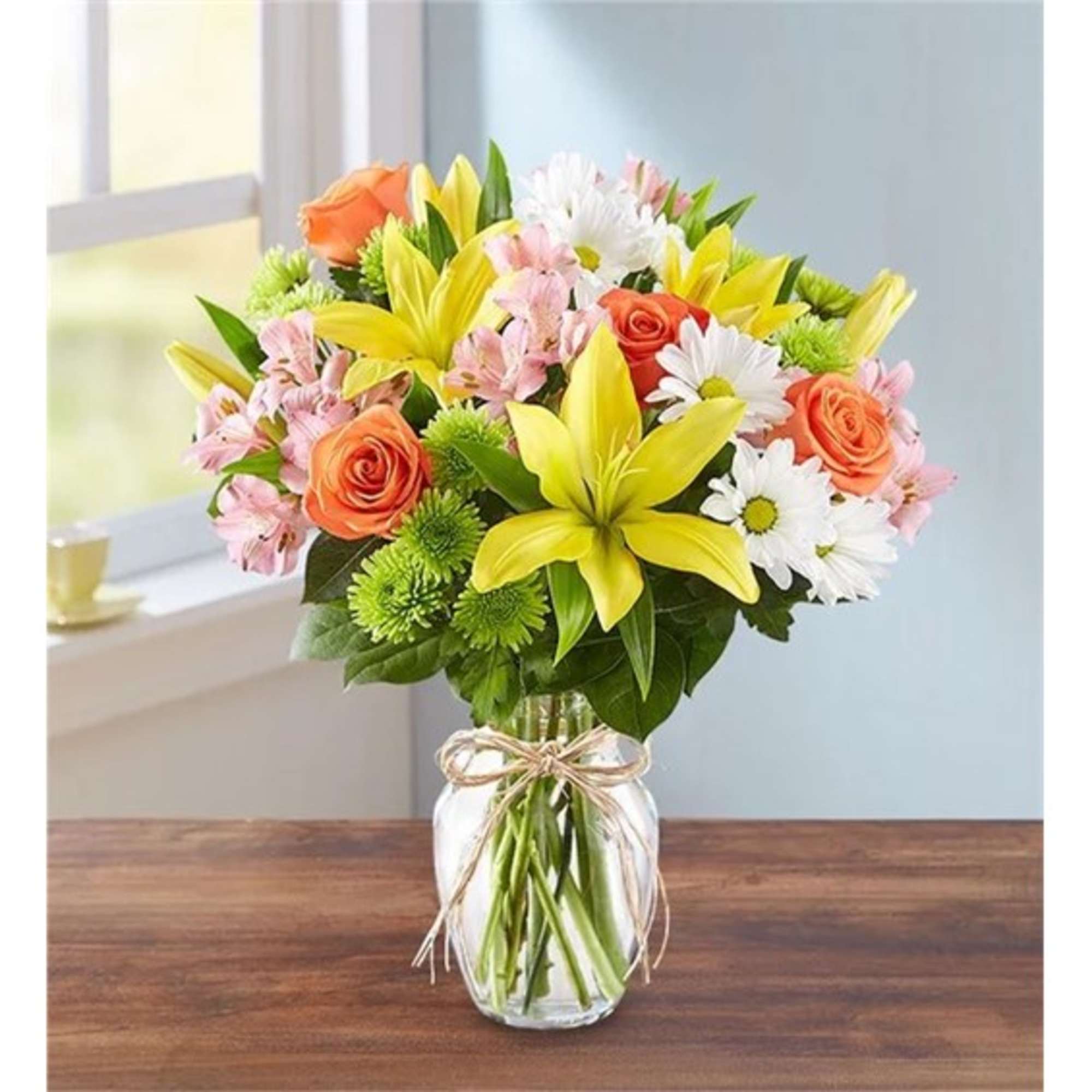 Bouquet of yellow lilies, orange roses, and white daisies in a glass vase