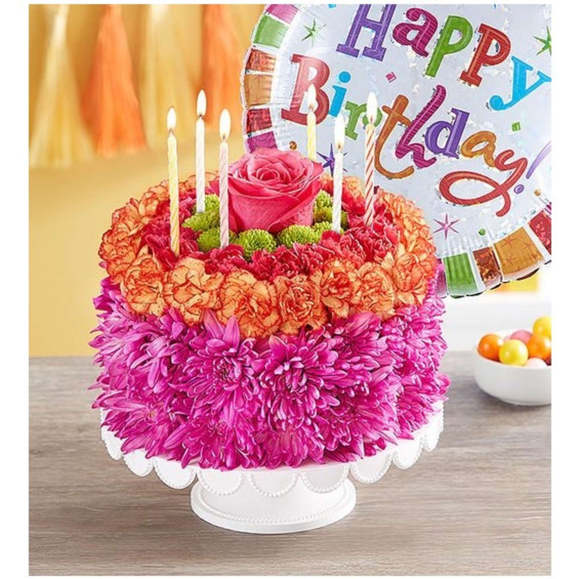 Flower-covered birthday cake with candles and a birthday balloon