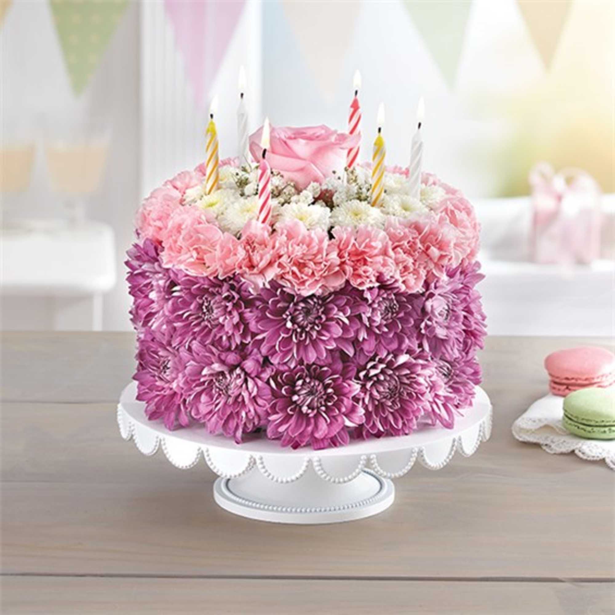 Pink and purple flower cake with striped candles on a white stand