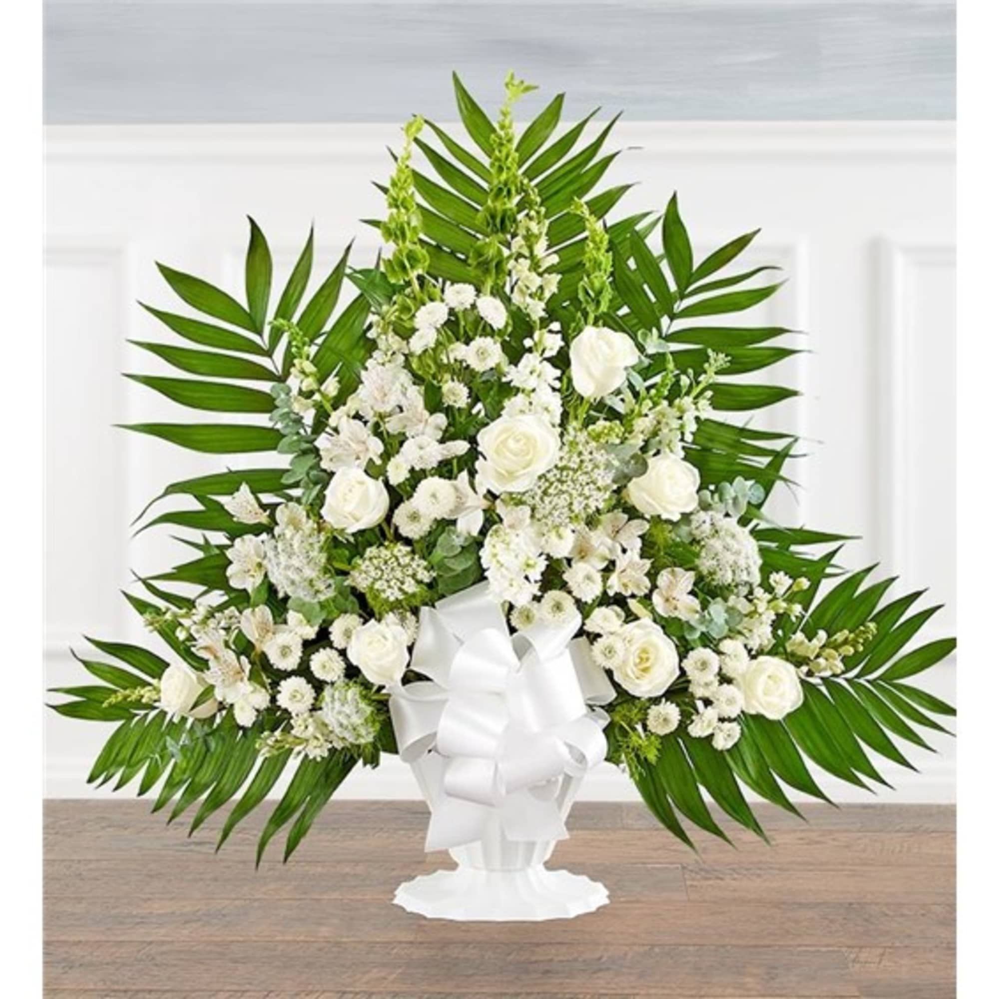White floral standing arrangement in a pedestal vase with a large bow