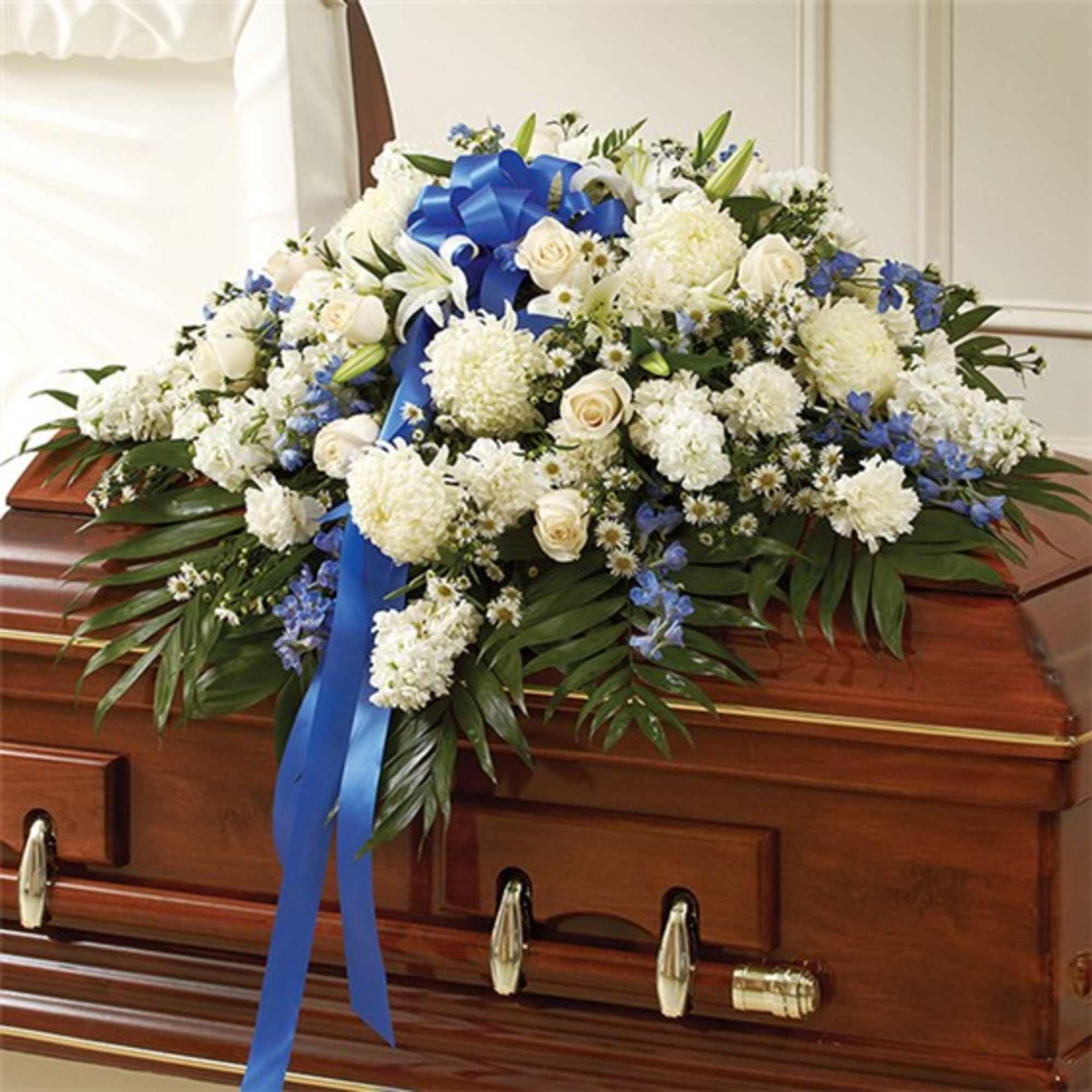 White and blue floral arrangement on a casket with a blue ribbon