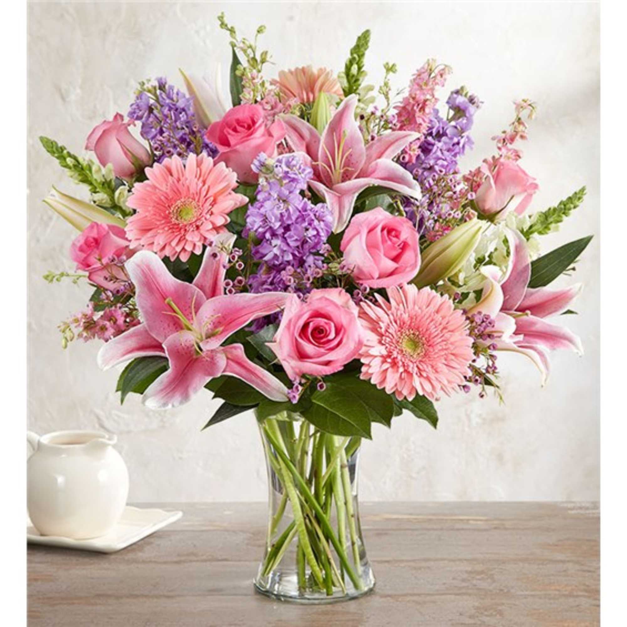 Pink roses, lilies, and gerbera daisies in a clear glass vase