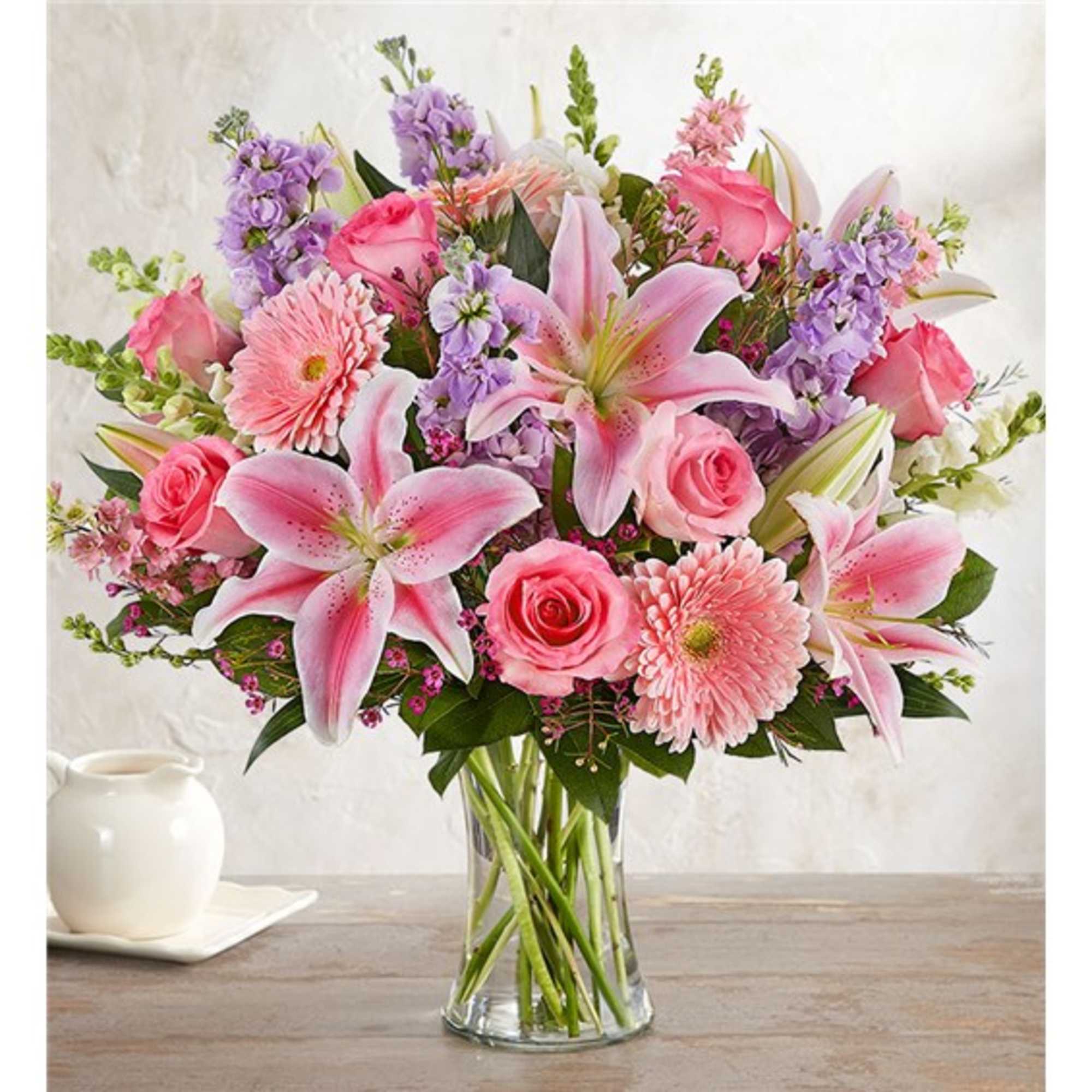 Pink lilies, roses, and daisies arranged in a clear glass vase