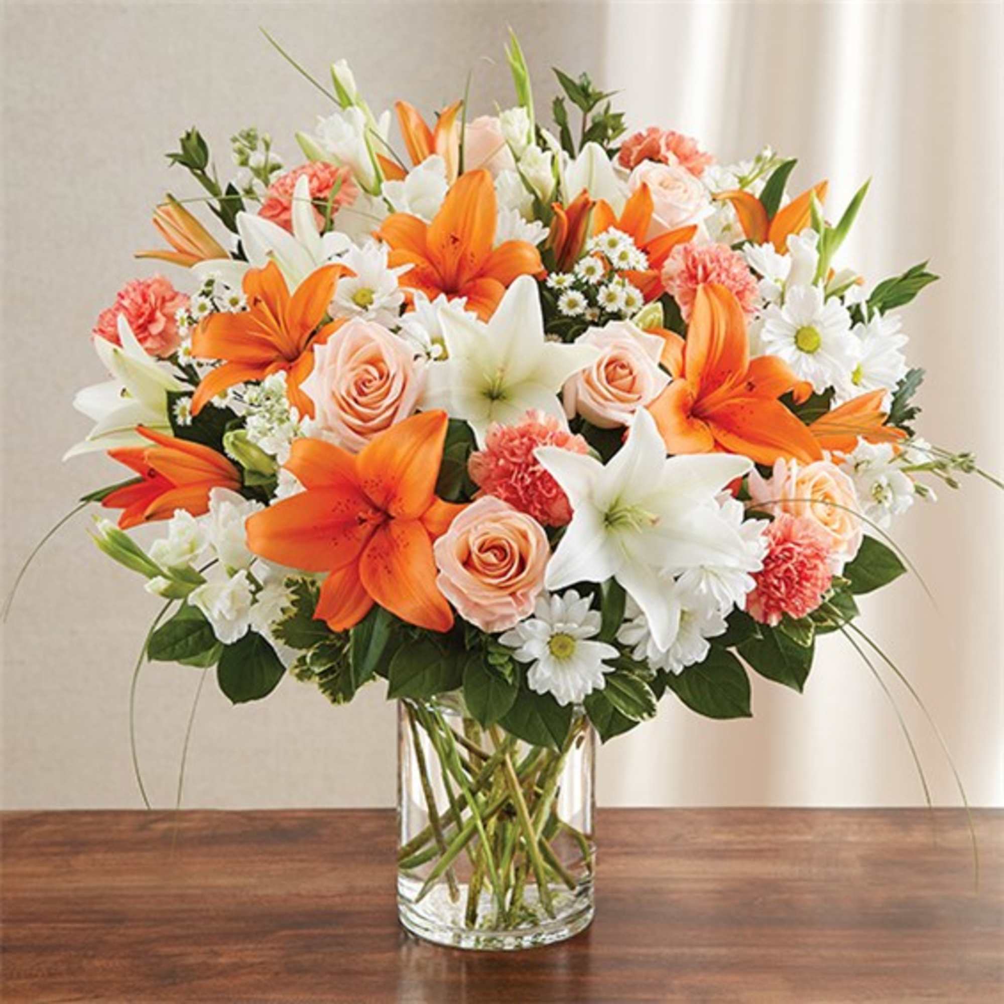 Bouquet of orange lilies, white lilies, pink roses, and daisies in a clear glass vase