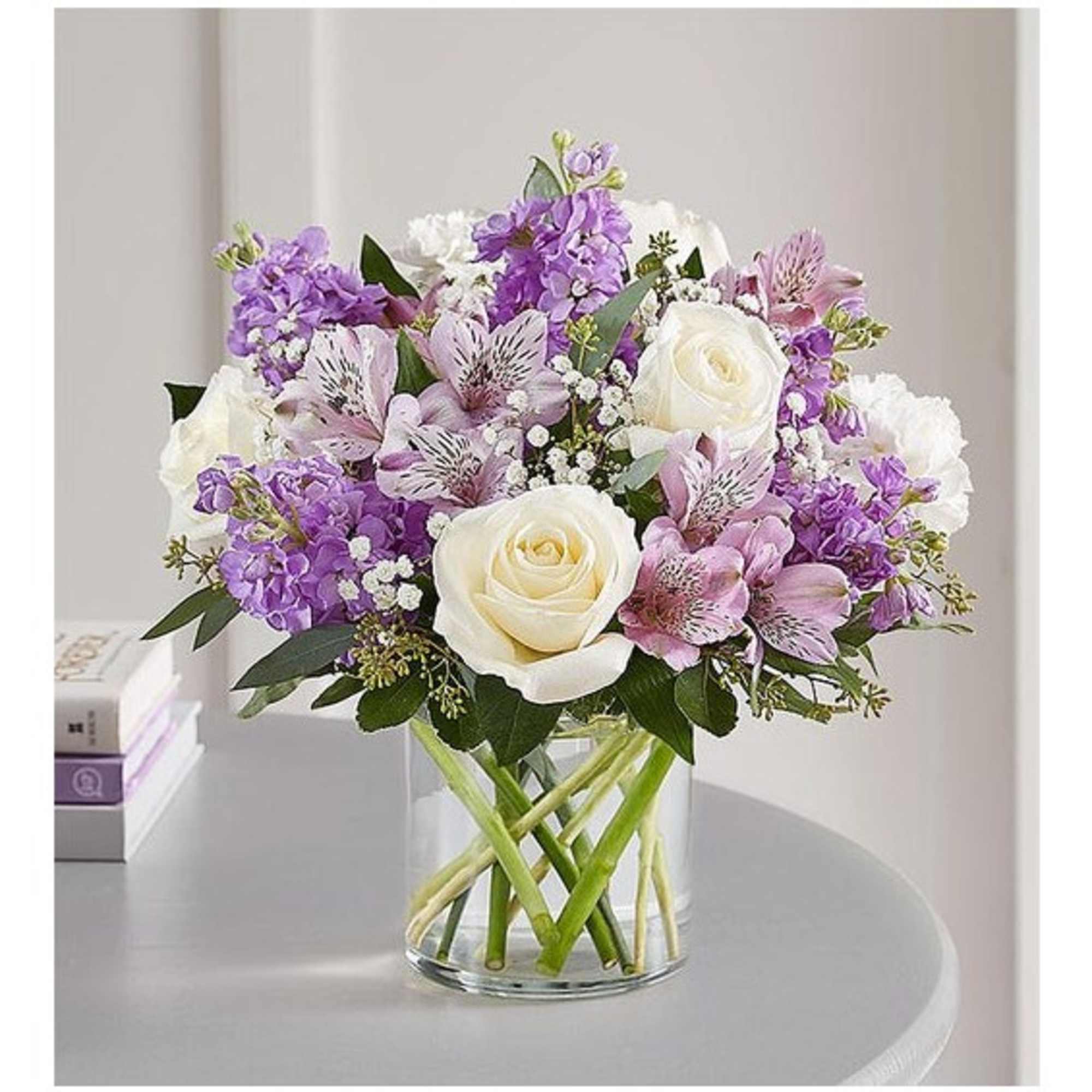 Bouquet of white roses and purple flowers in a clear glass vase