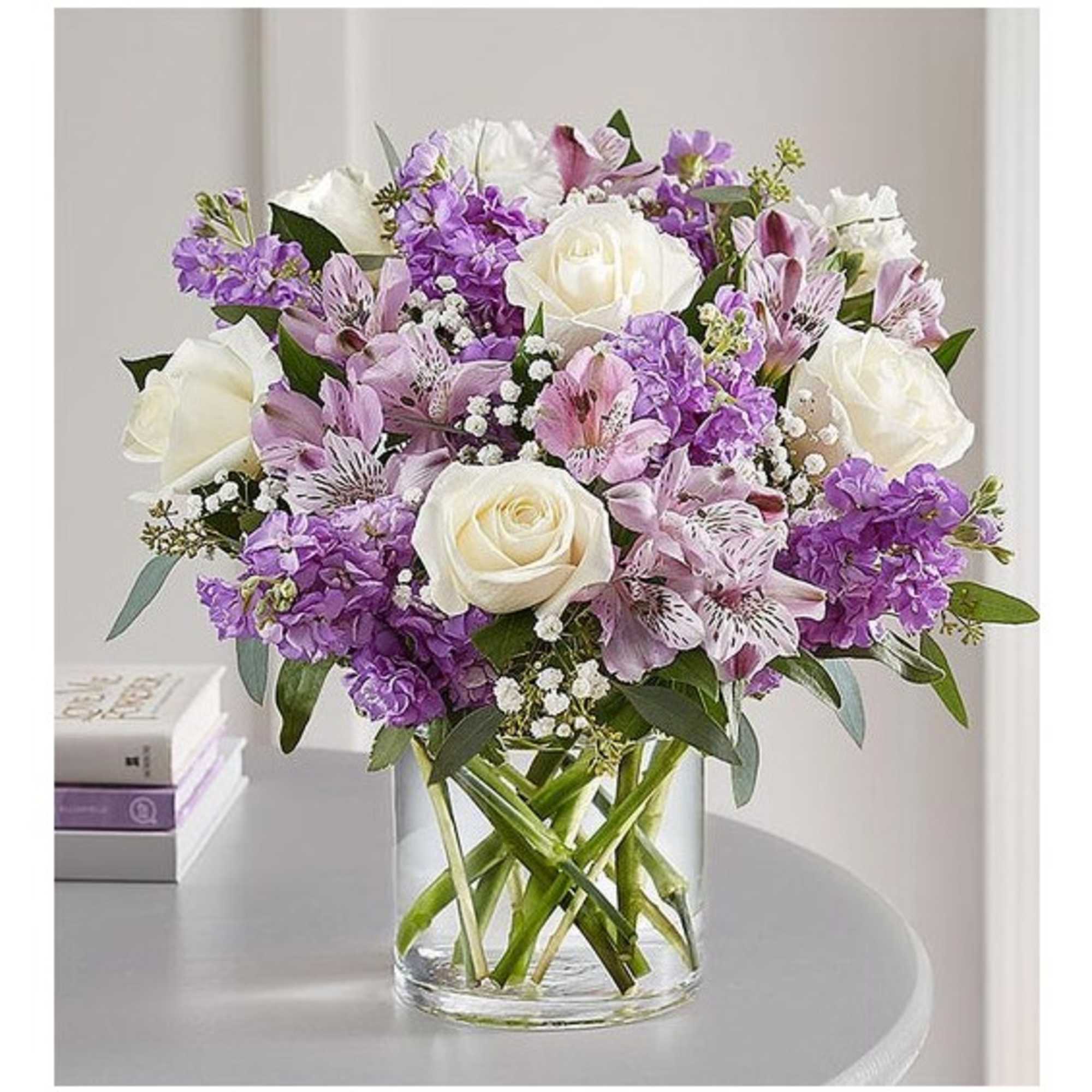 Bouquet of white roses and purple flowers in a clear glass vase