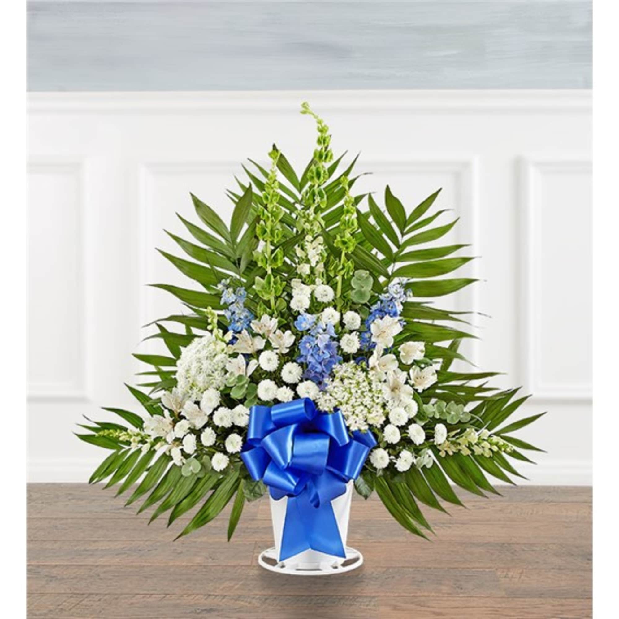 Standing floral arrangement with white and blue flowers and a blue ribbon in a white container