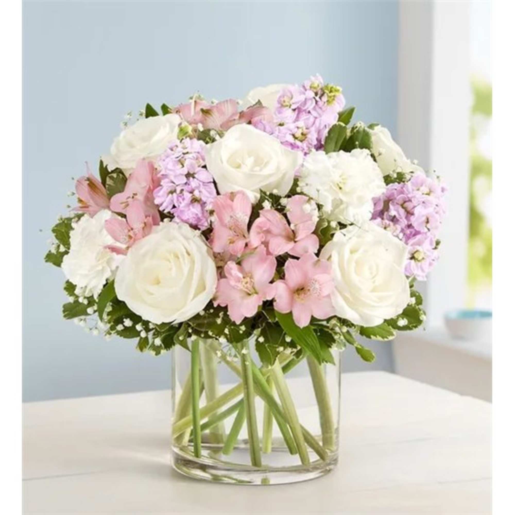 Bouquet of white roses, pink flowers, and lavender blooms in a clear glass vase