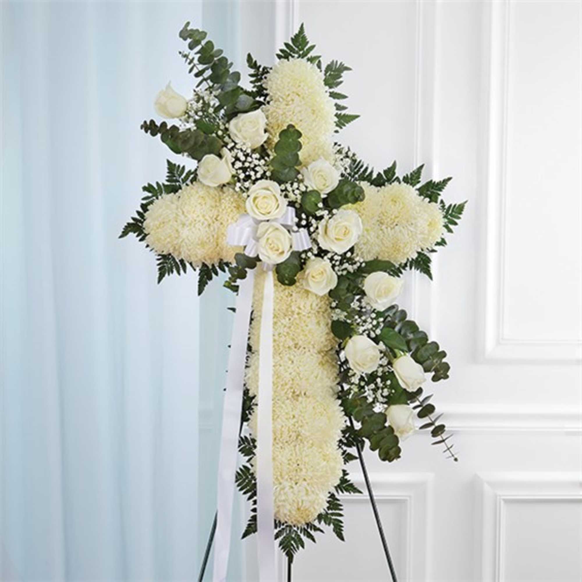 White floral cross arrangement with roses and ribbon on a stand