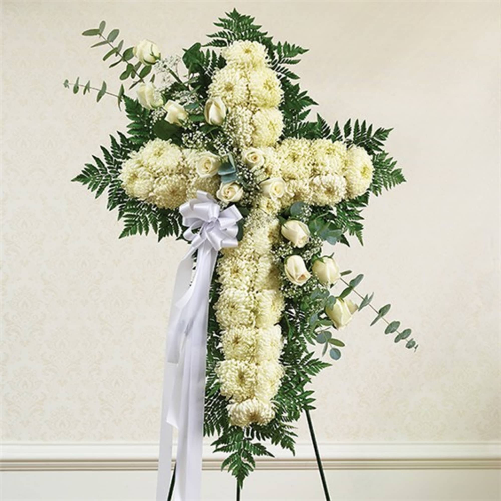 White floral cross arrangement with a ribbon bow on a stand