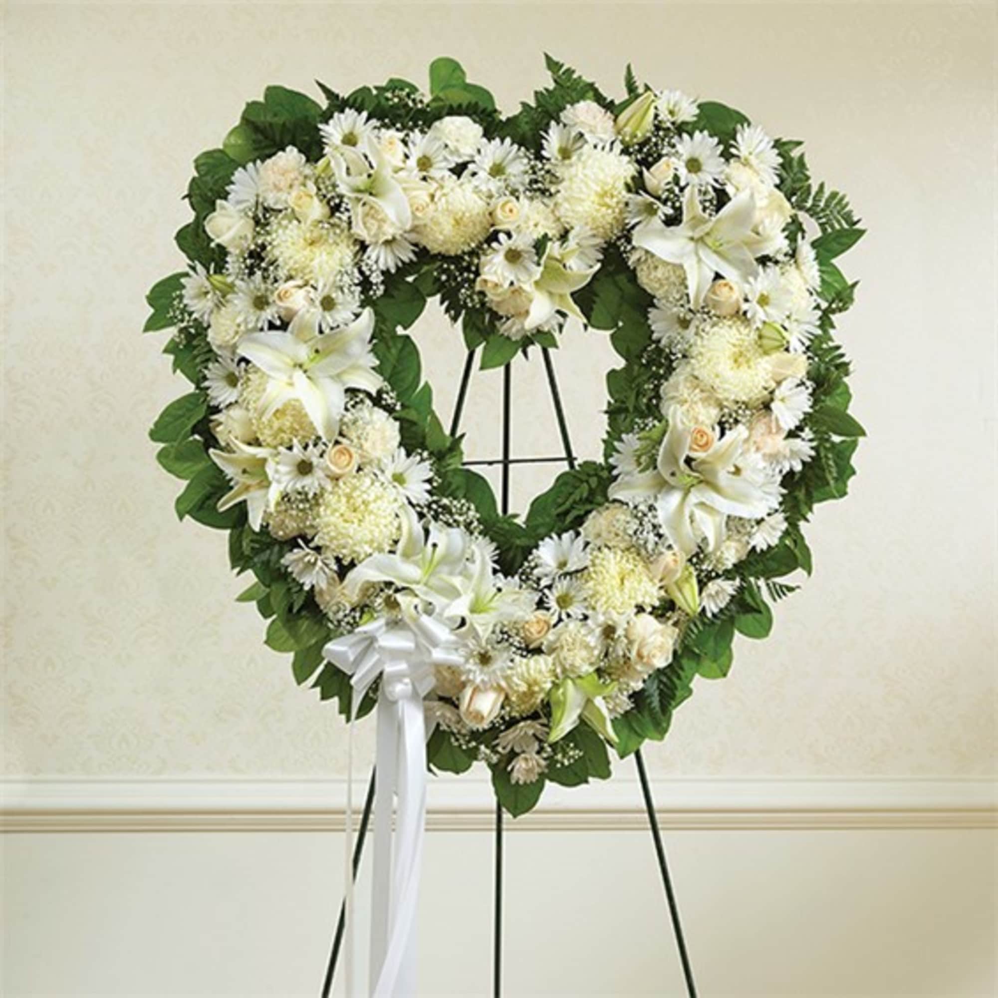 Heart-shaped white floral wreath on a stand with a white ribbon