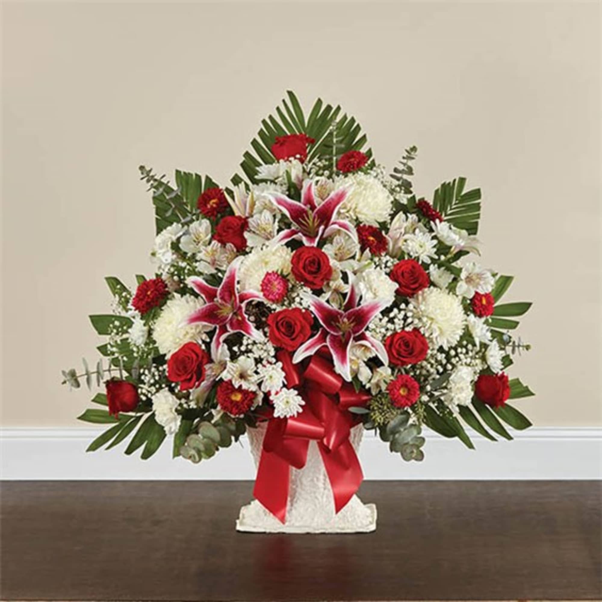 Red and white floral arrangement in a white vase with a red ribbon