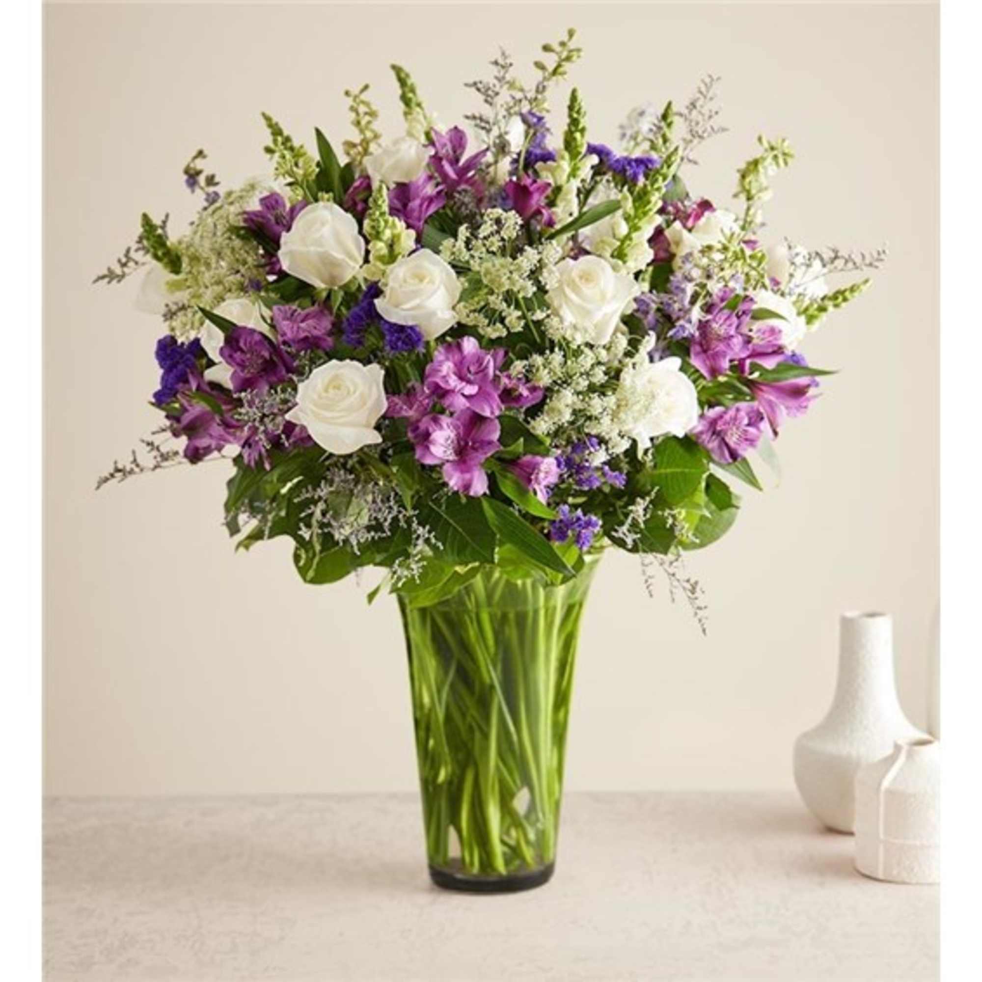 Bouquet of white roses and purple flowers in a tall glass vase
