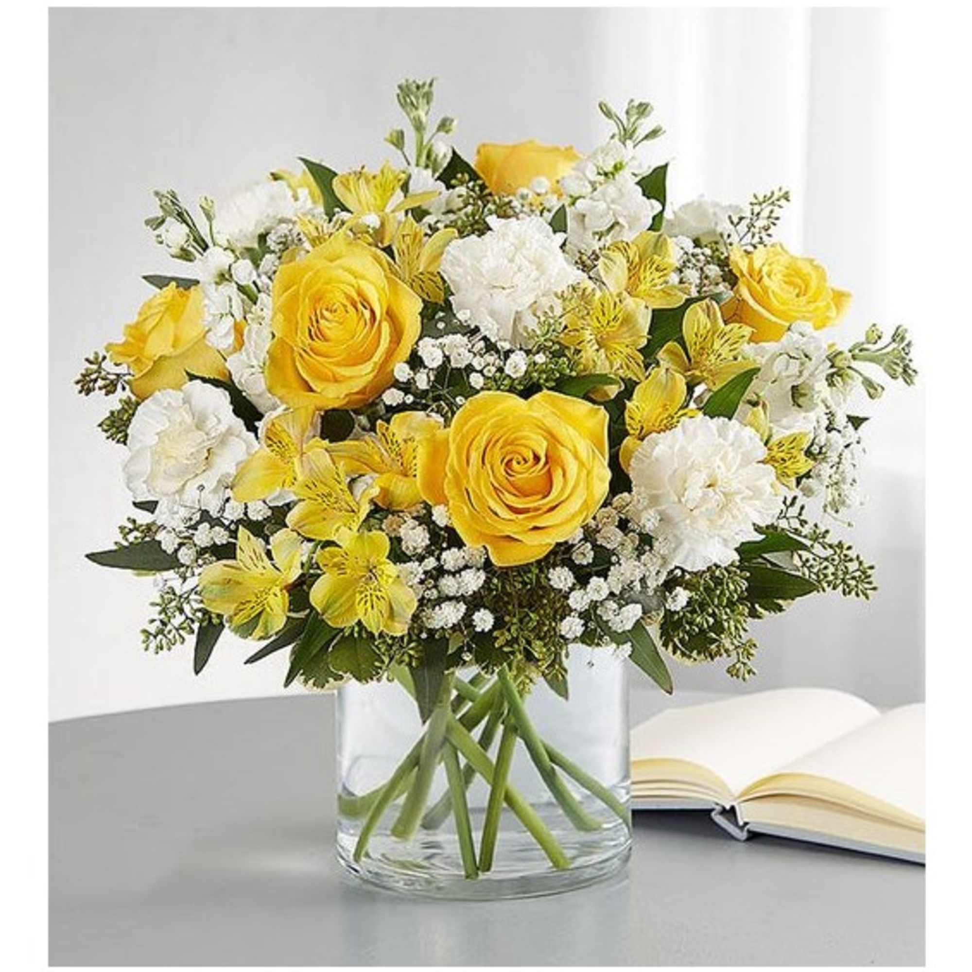 Yellow roses and white flowers arranged in a clear glass vase