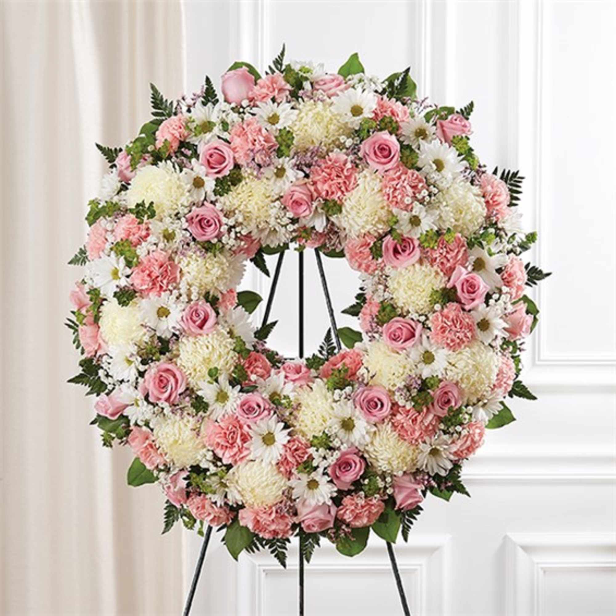Heart-shaped floral wreath with pink roses and white daisies on a stand