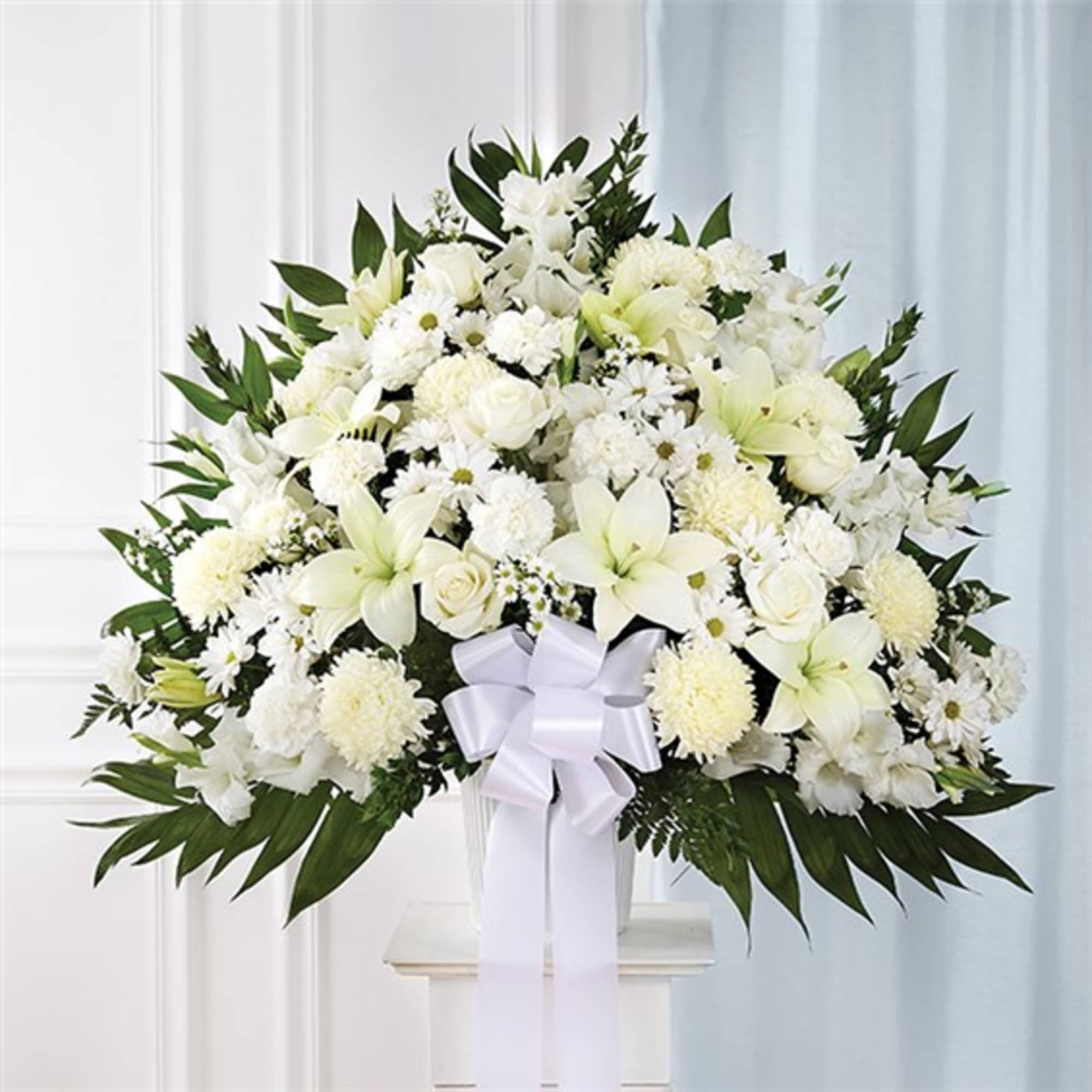 Large white floral arrangement with lilies and roses in a vase, tied with a white ribbon