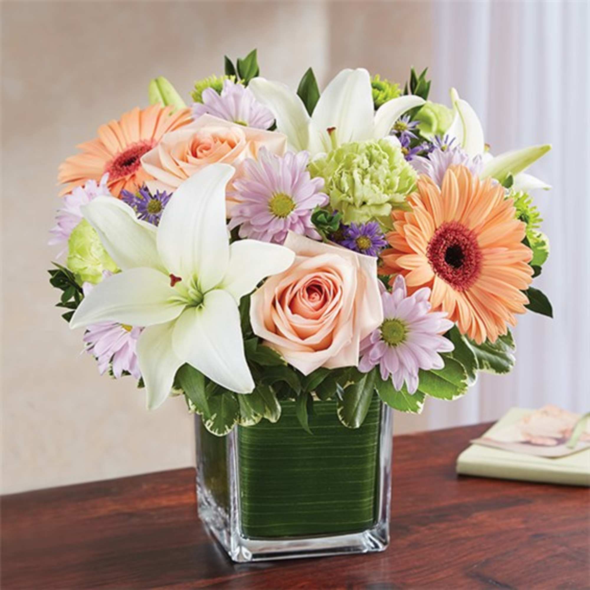 Mixed bouquet of lilies, roses, and daisies in a square glass vase