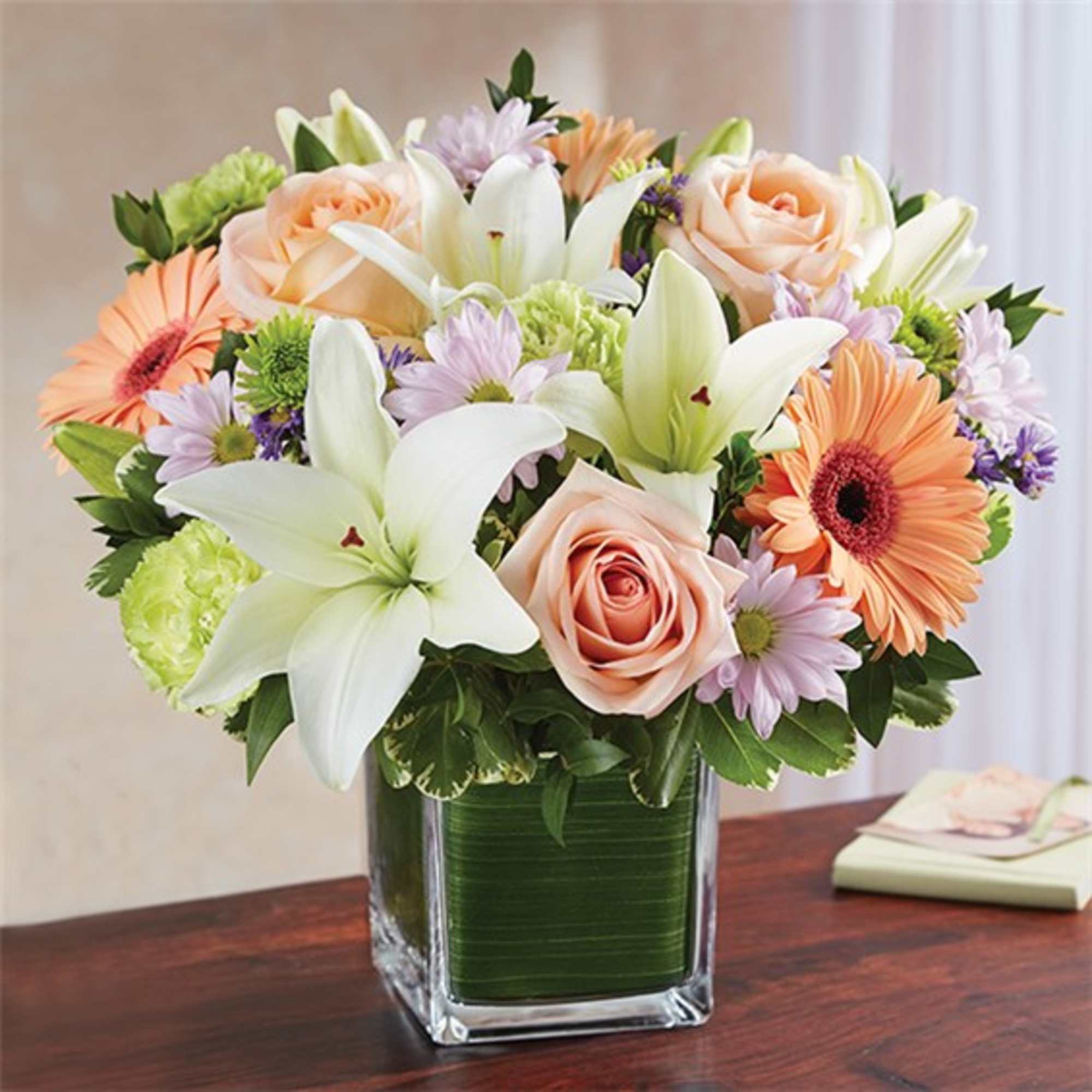 Mixed bouquet of lilies, roses, and daisies in a square glass vase