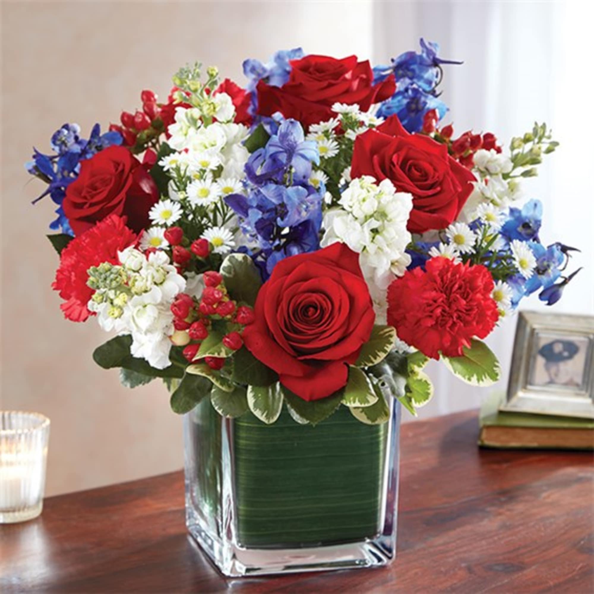 Bouquet of red roses, blue flowers, and white blooms in a square glass vase