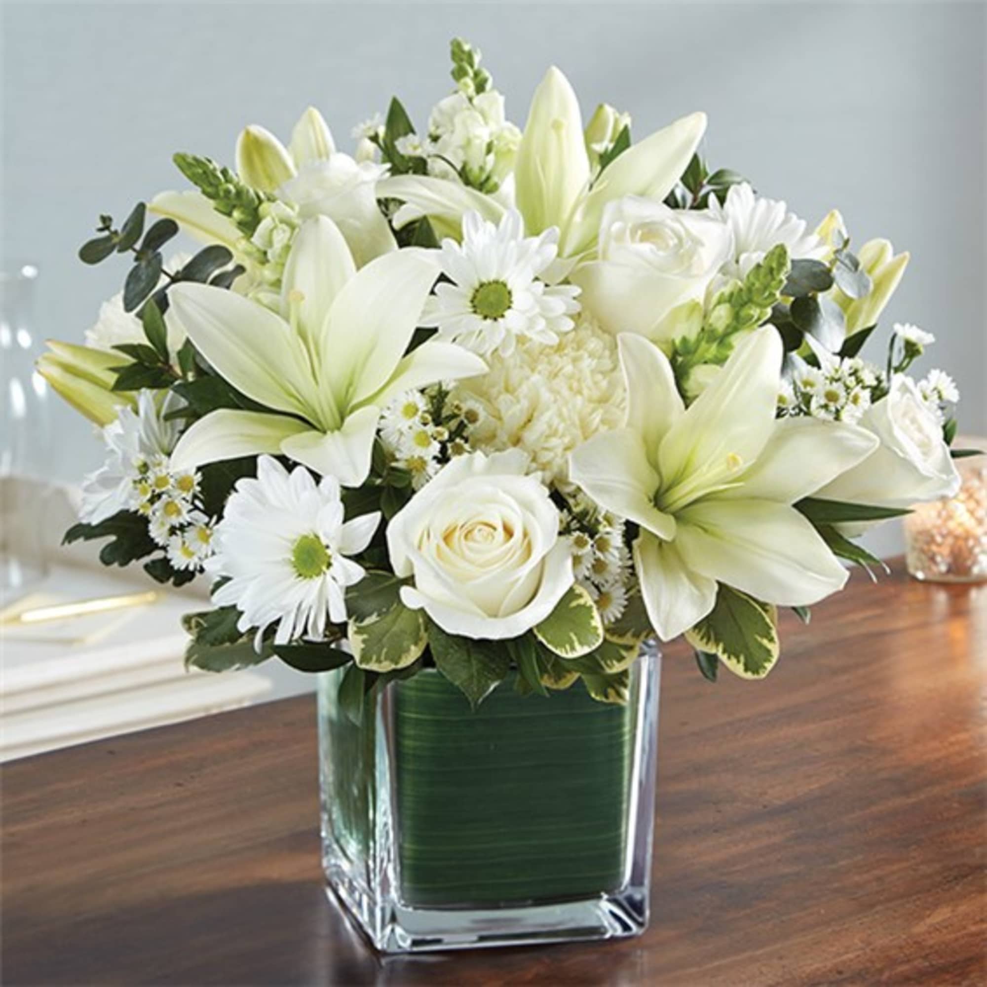 White lilies and roses arranged in a square glass vase