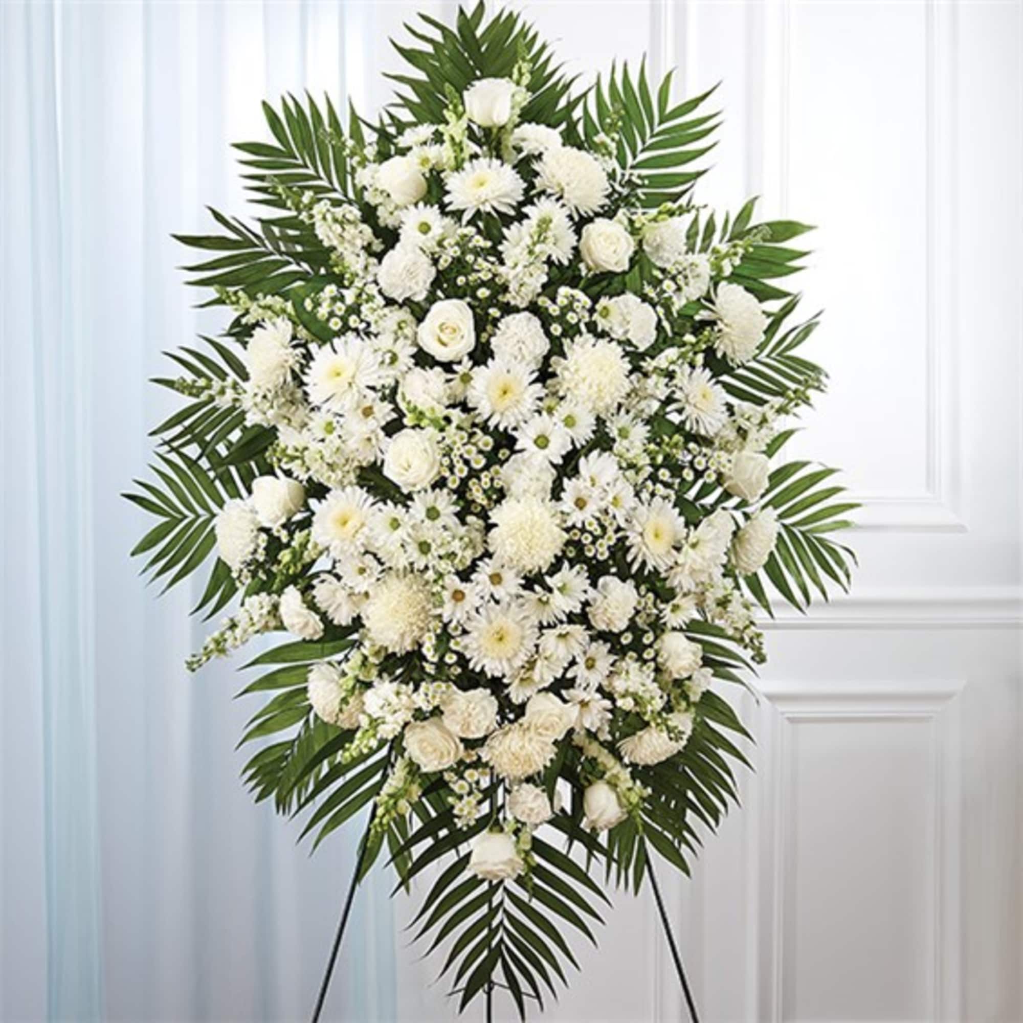 White funeral spray with mixed blooms and palm fronds on an easel