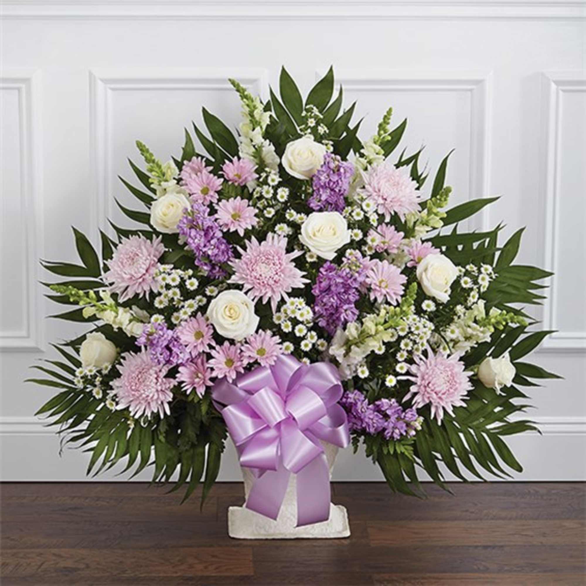 Lavender and white floral arrangement in a white container with a purple bow