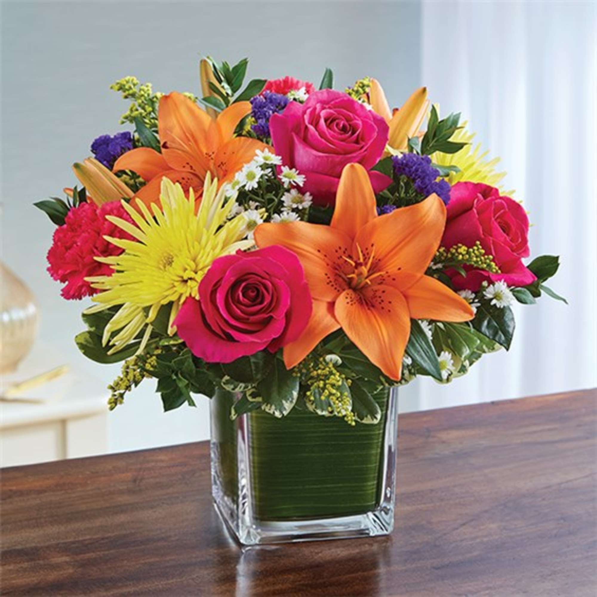 Bright mixed bouquet in a square glass vase with roses, lilies, and mums