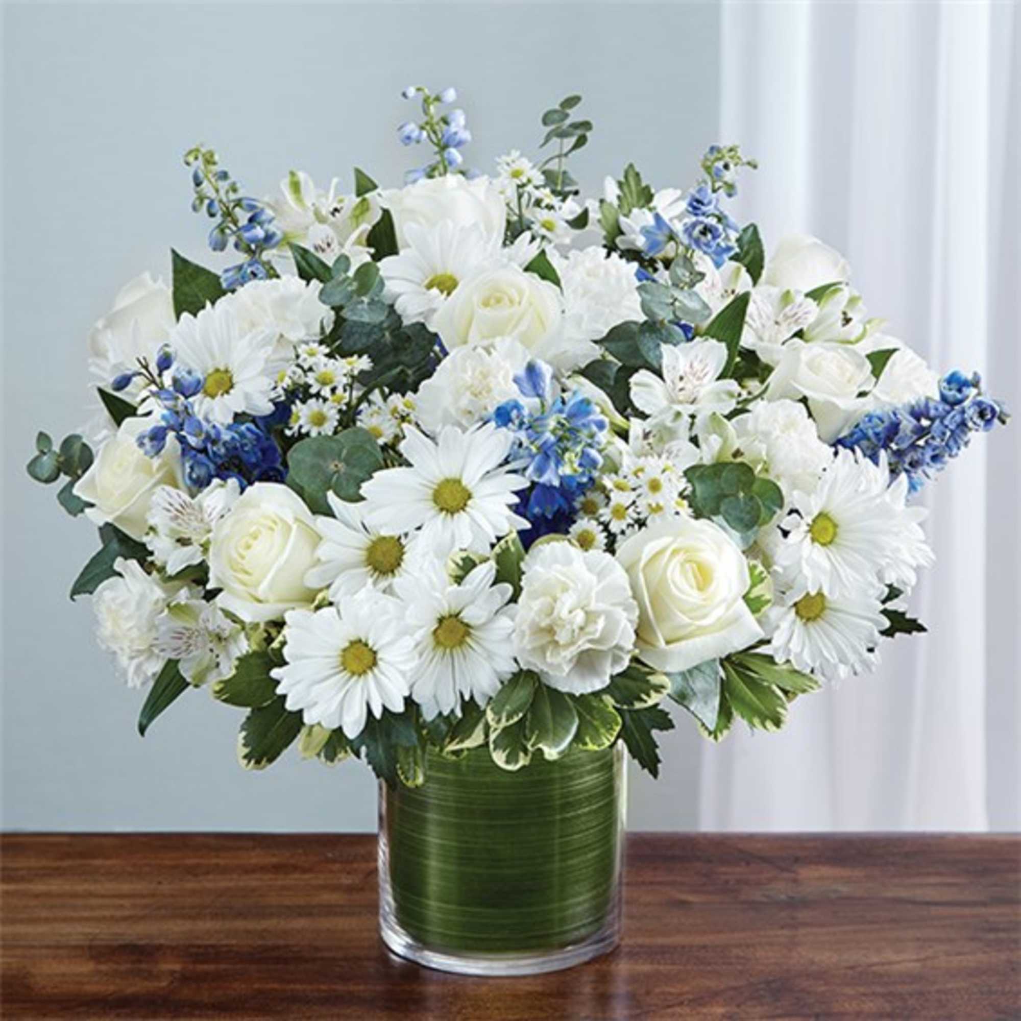 White daisies and roses in a clear glass vase with blue accents