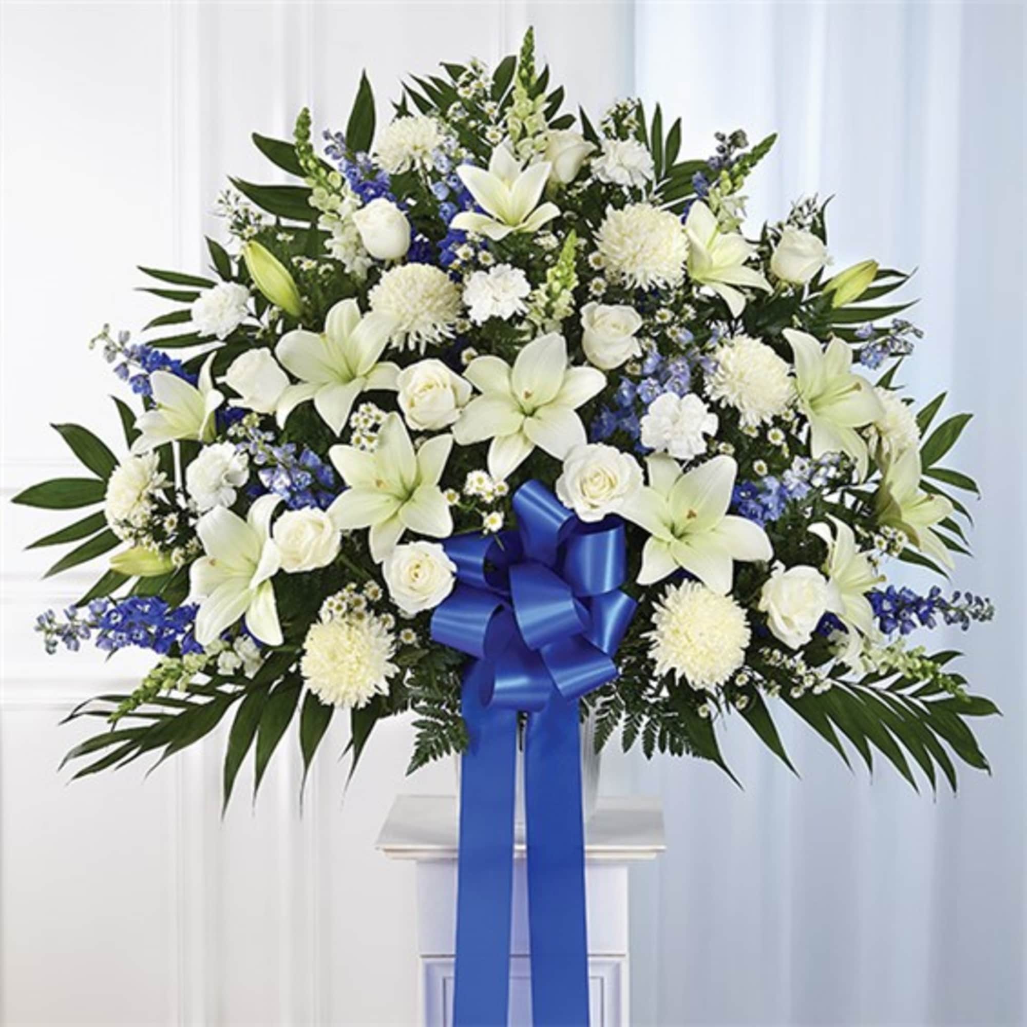 White lilies and roses in a large standing arrangement with a blue ribbon