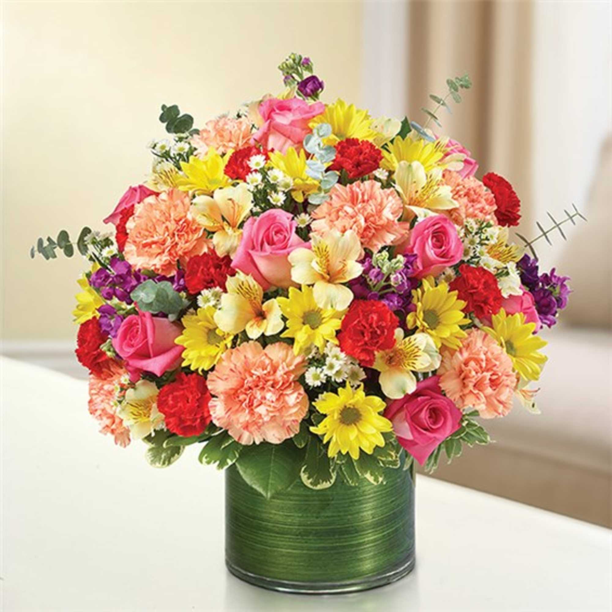 Mixed bouquet of pink roses, yellow daisies, and carnations in a green vase