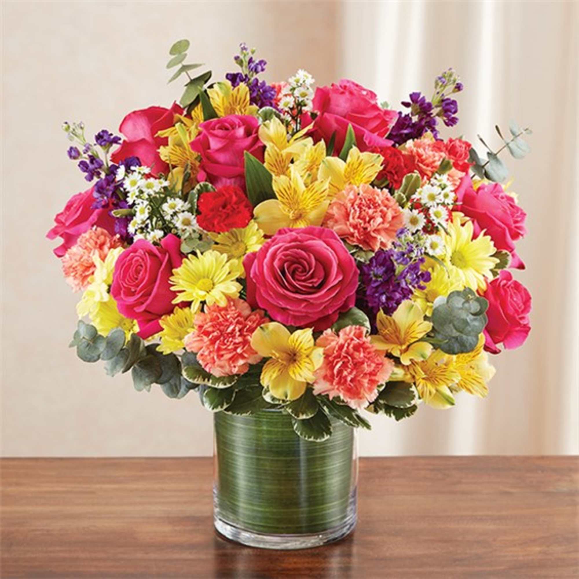 Mixed bouquet of pink roses, yellow daisies, and carnations in a glass vase