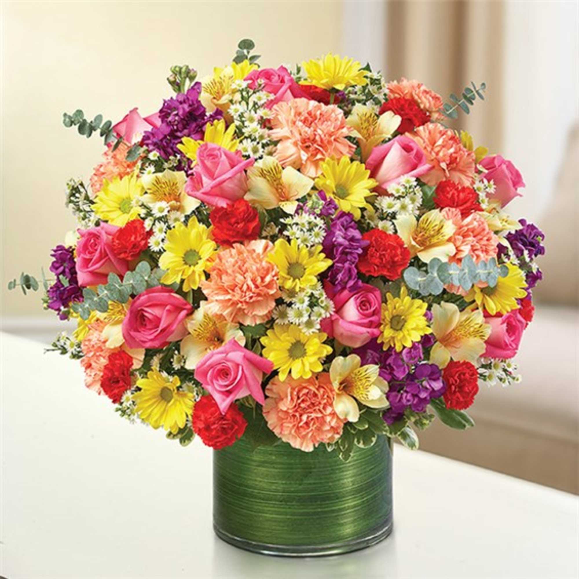 Mixed bouquet of pink, yellow, purple, and peach flowers in a green vase