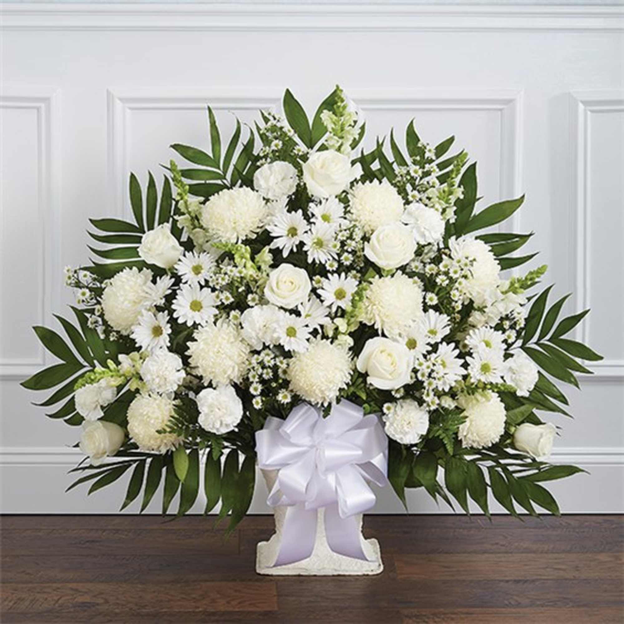 White floral arrangement in a pedestal vase with a white ribbon