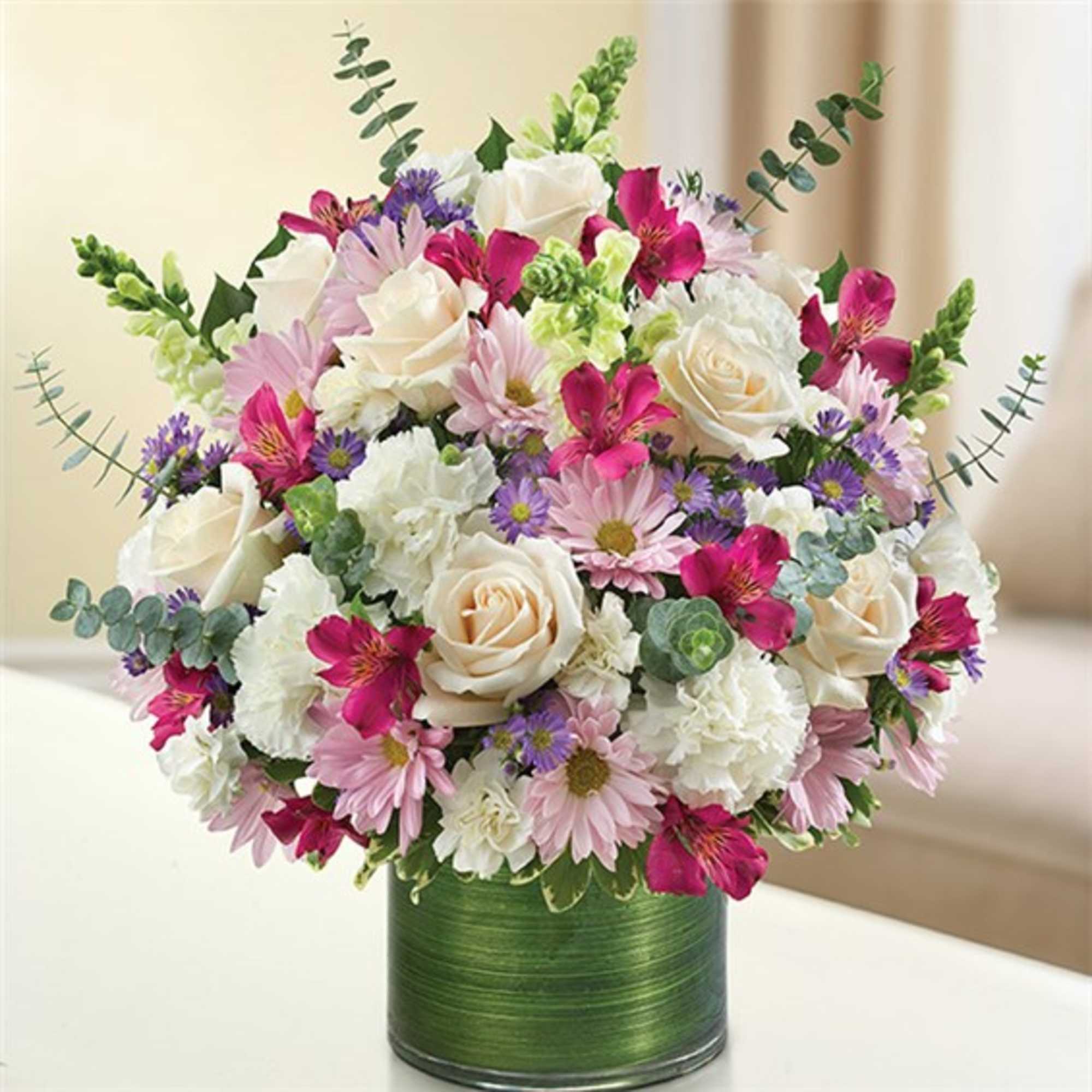 Mixed bouquet of white roses, pink daisies, and purple flowers in a green vase