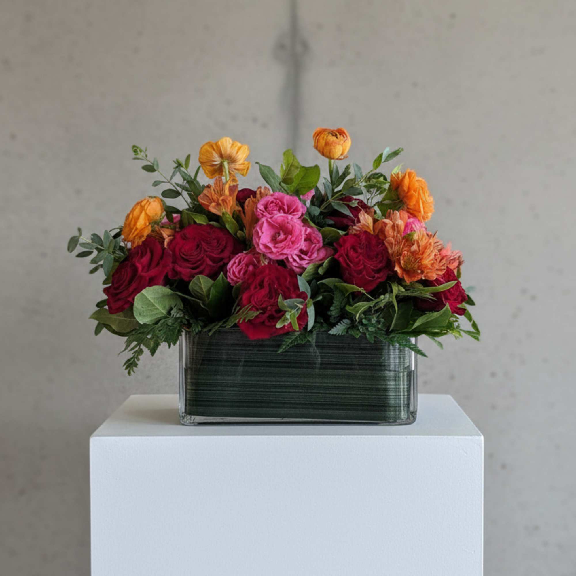 Mixed bouquet of red, pink, and orange flowers in a rectangular glass vase