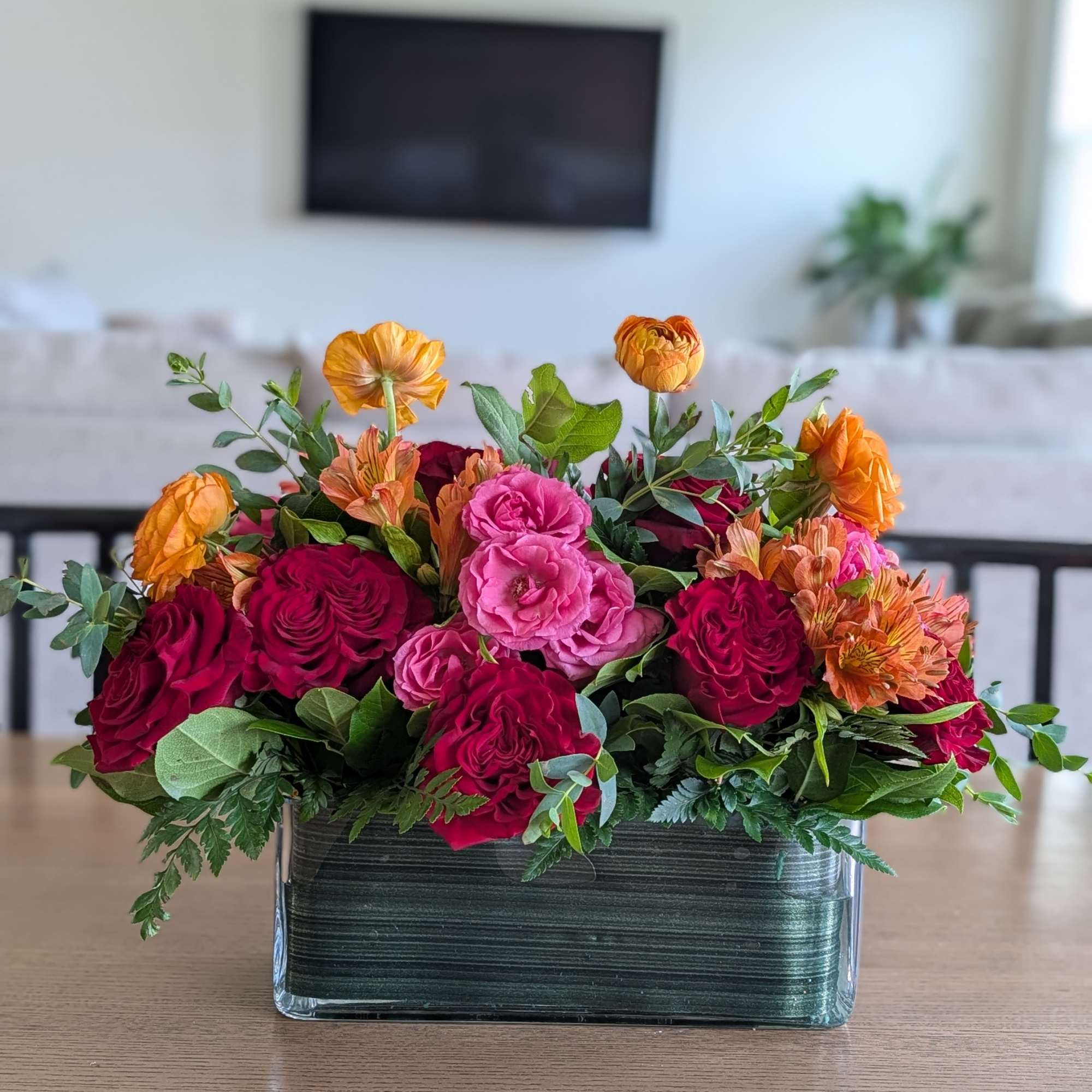 Low floral arrangement of pink, red, and orange blooms in a rectangular glass vase.
