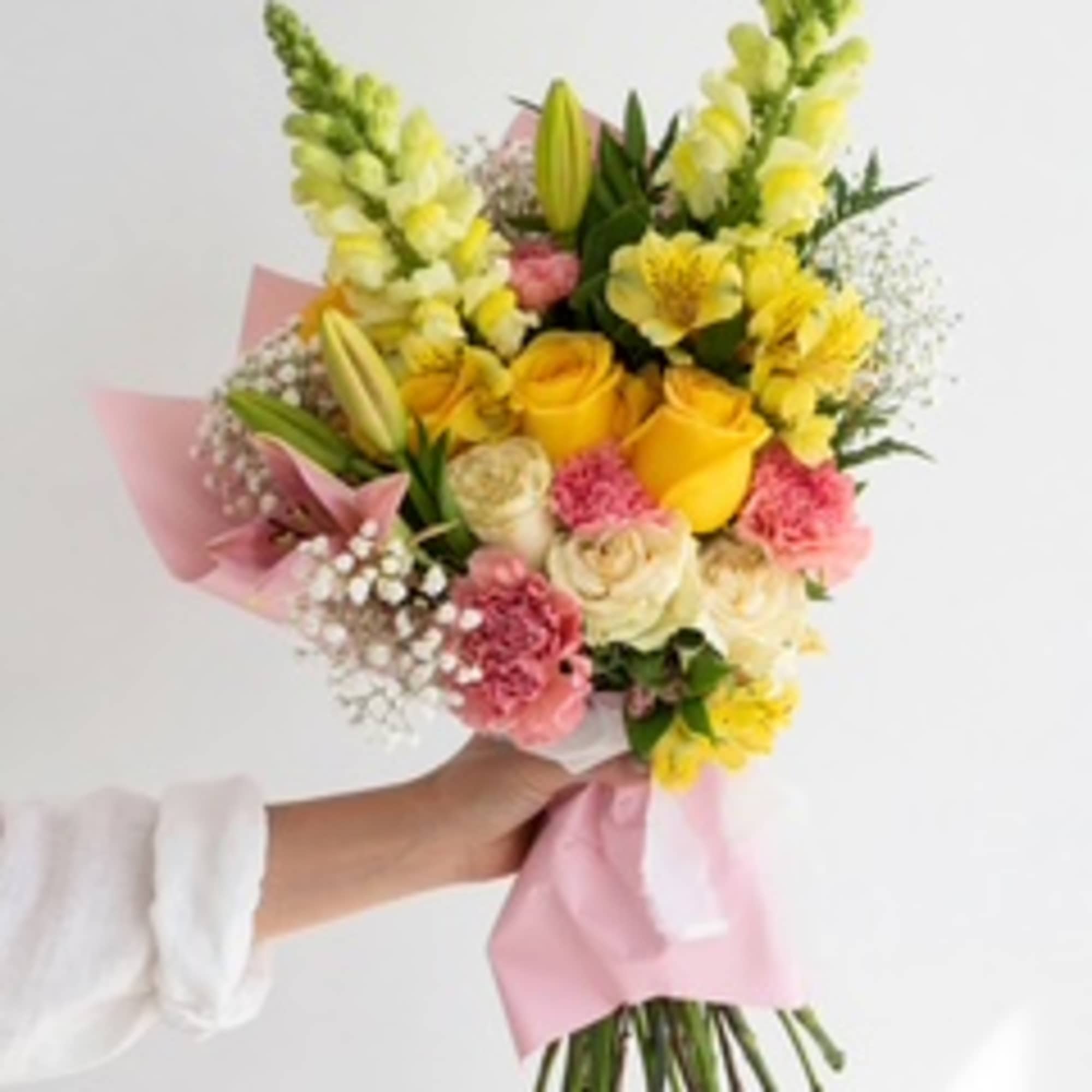 Handheld bouquet of yellow roses, lilies, and pink carnations wrapped in pink paper