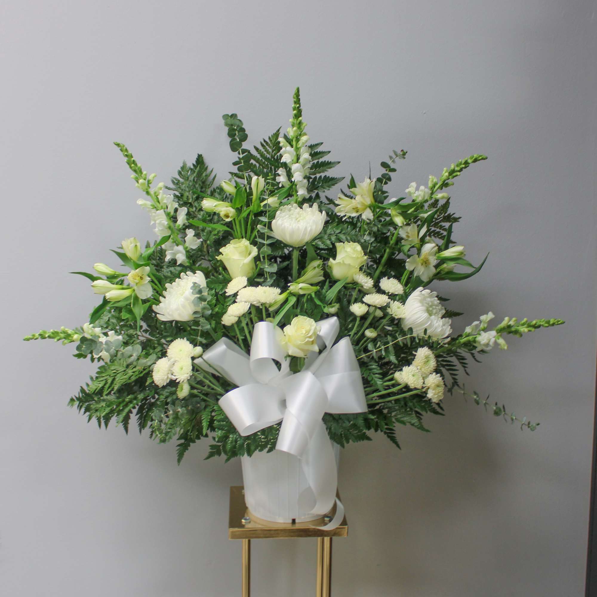 White floral arrangement in a vase with a large white ribbon bow