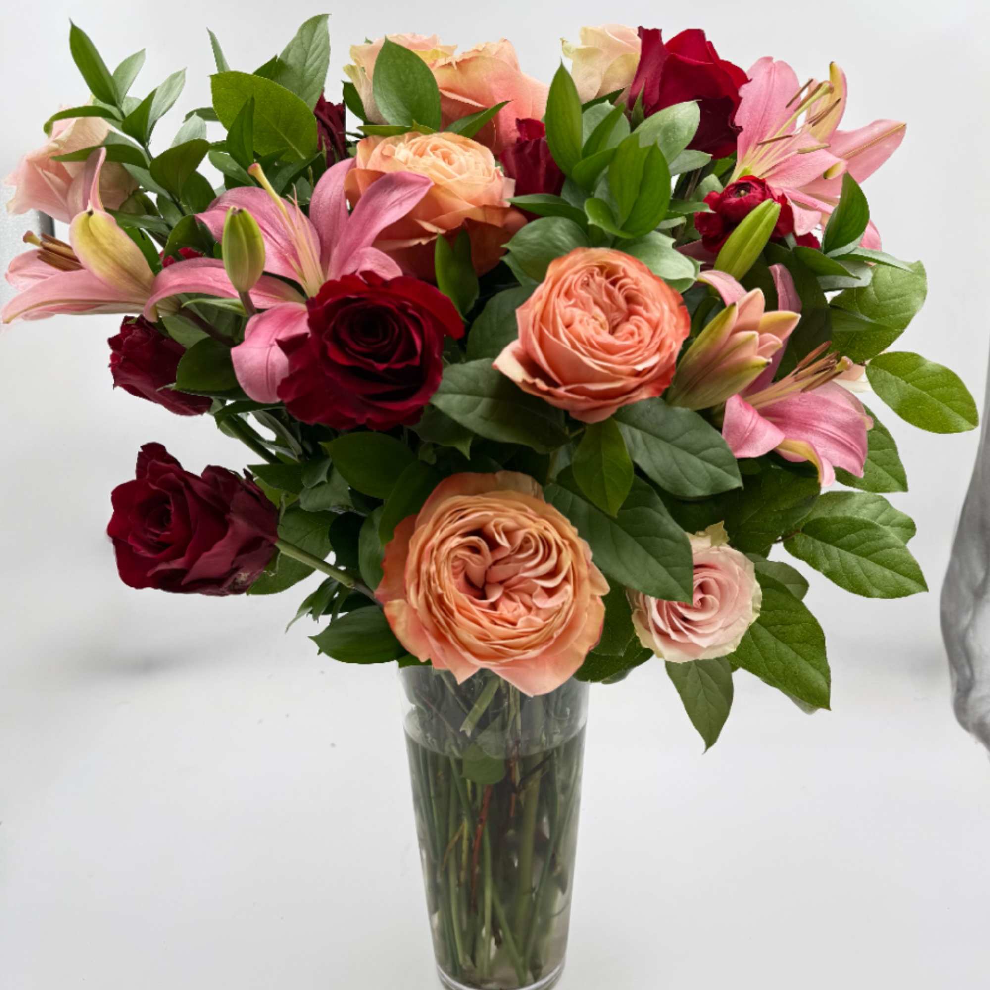 Bouquet of pink, peach, and red roses with lilies in a clear glass vase