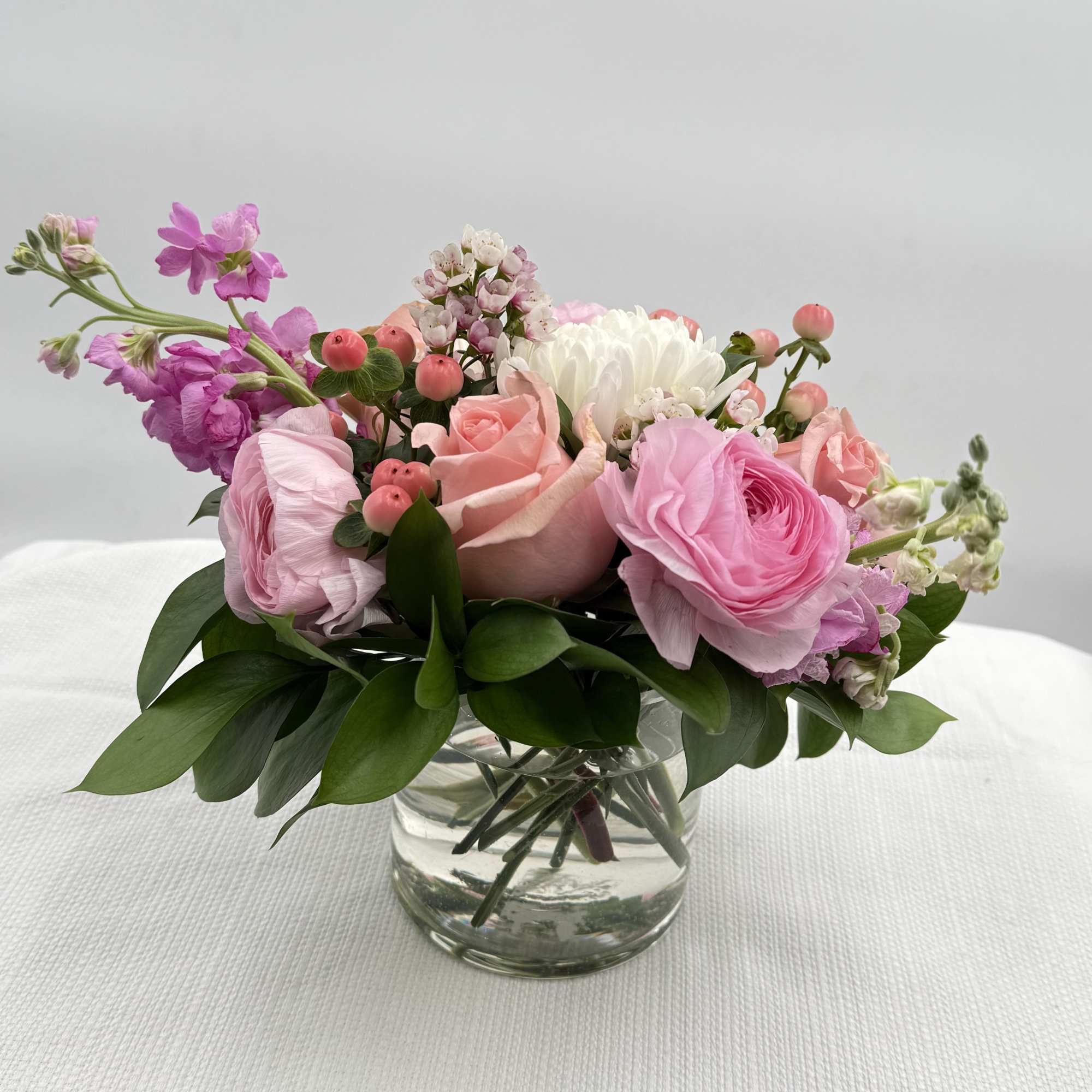 Low arrangement of soft pink and white roses and ranunculus in a clear glass vase.