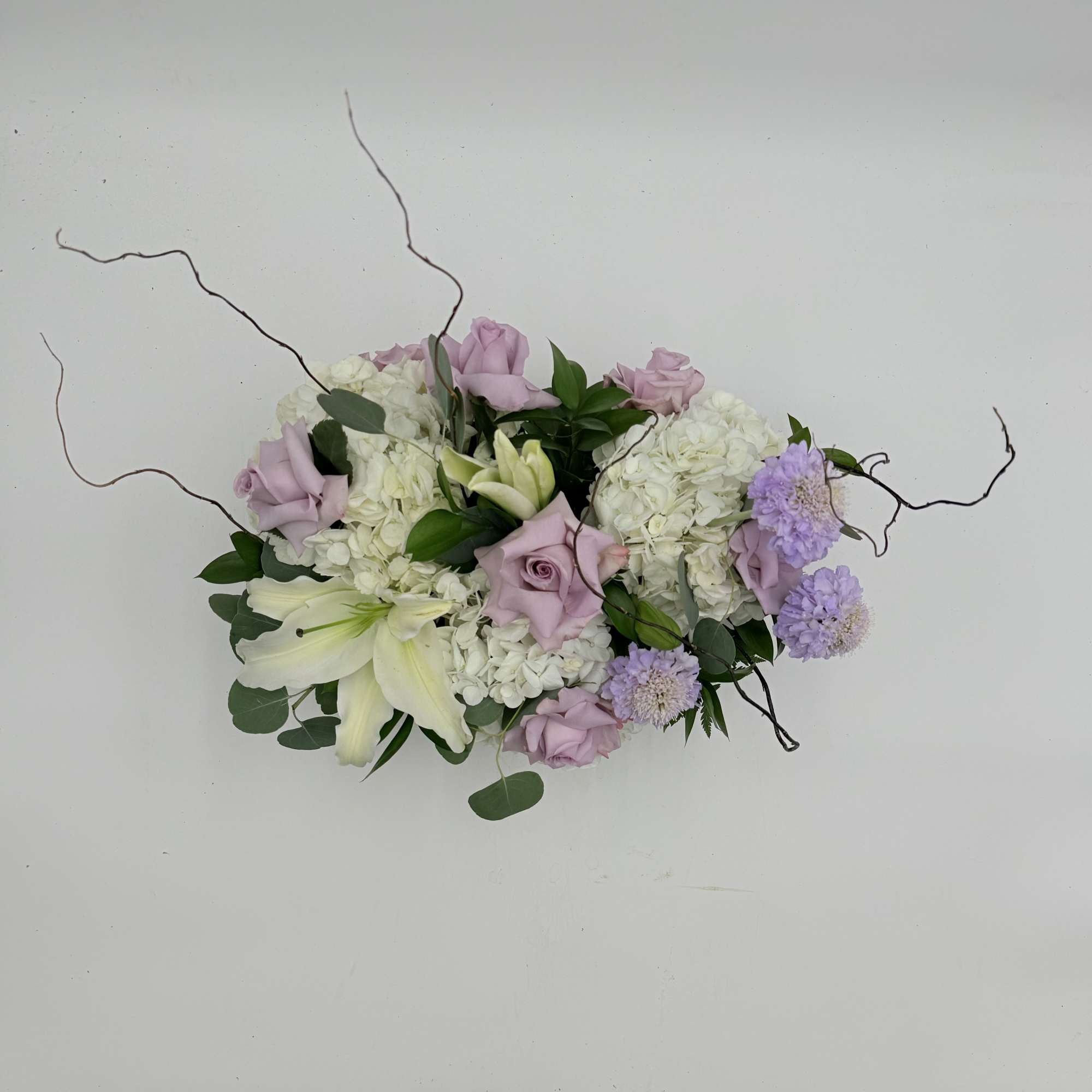 Lavender roses and white lilies arranged with white hydrangeas and purple accents