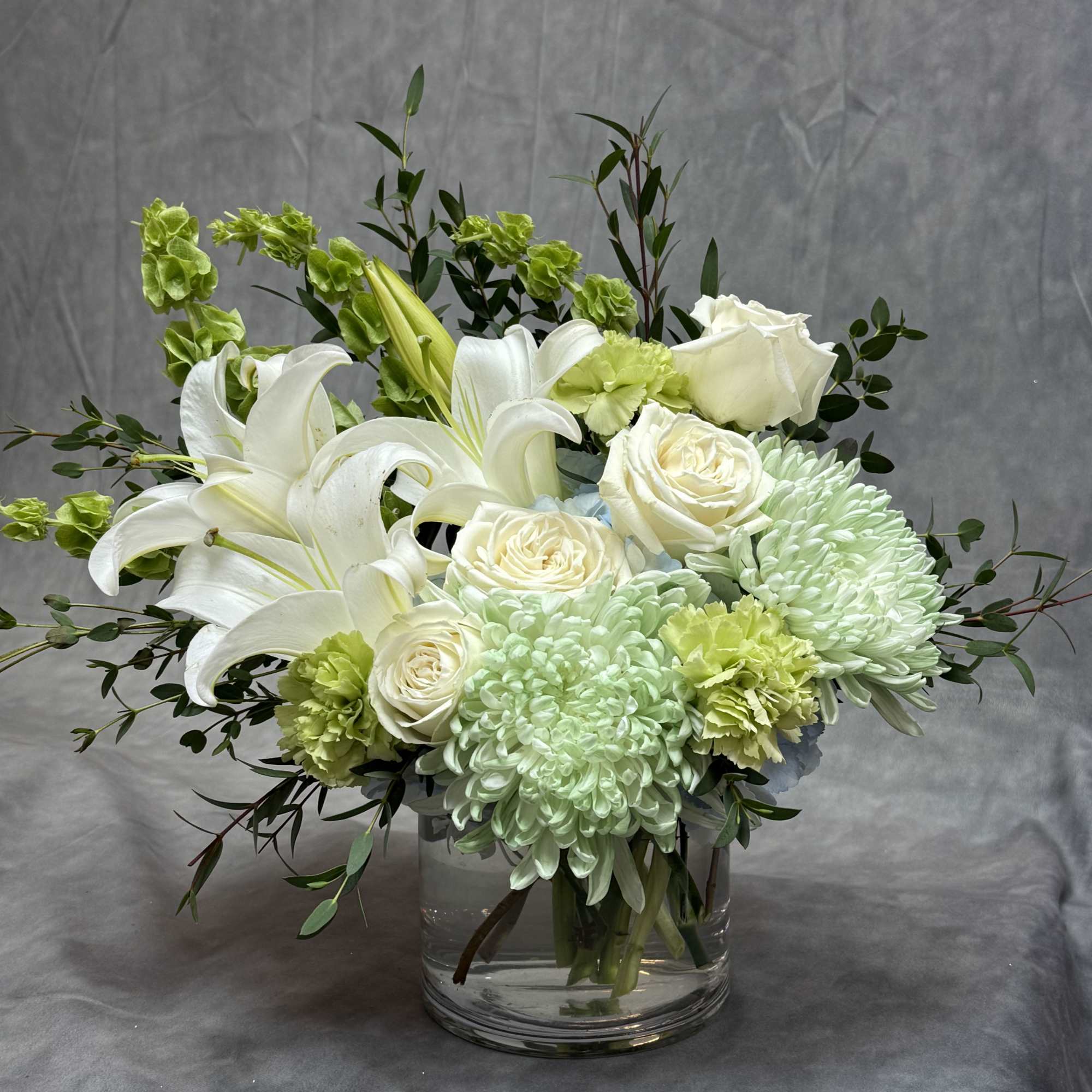 White lilies and roses in a clear glass vase with pale green blooms